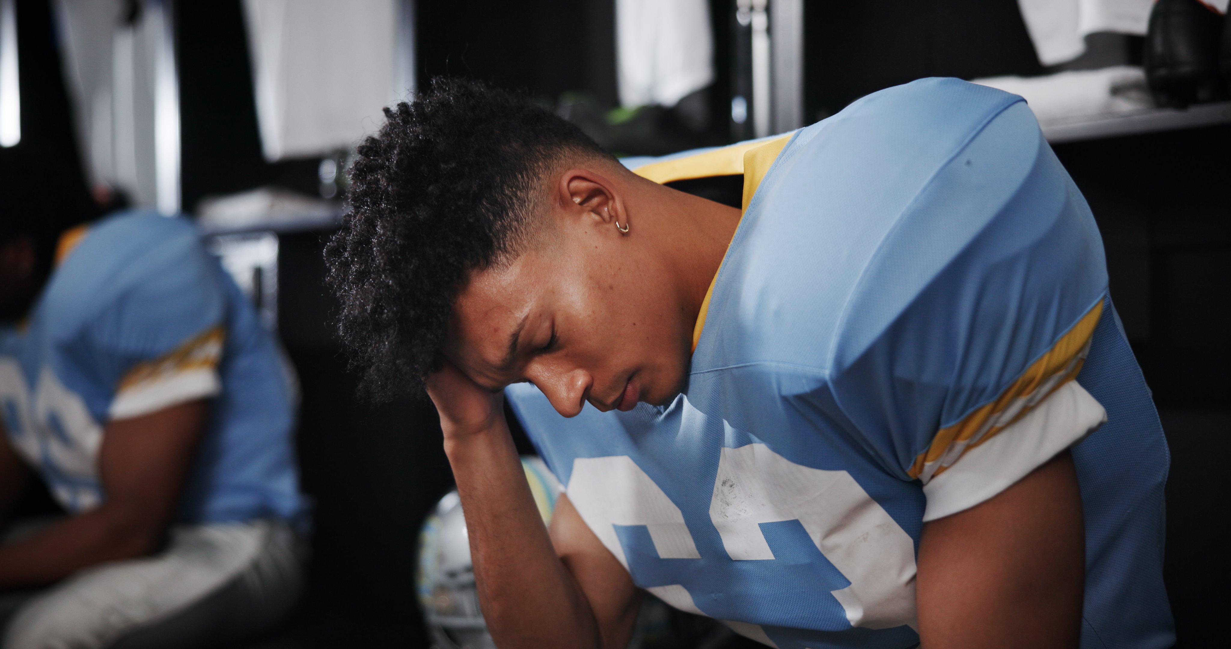 Football player on sidelines holds head 