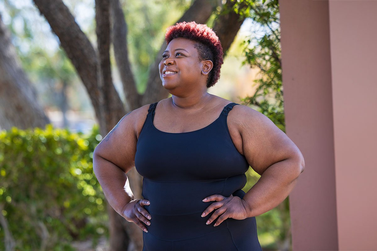 Person standing outside smiling with hands on hips.