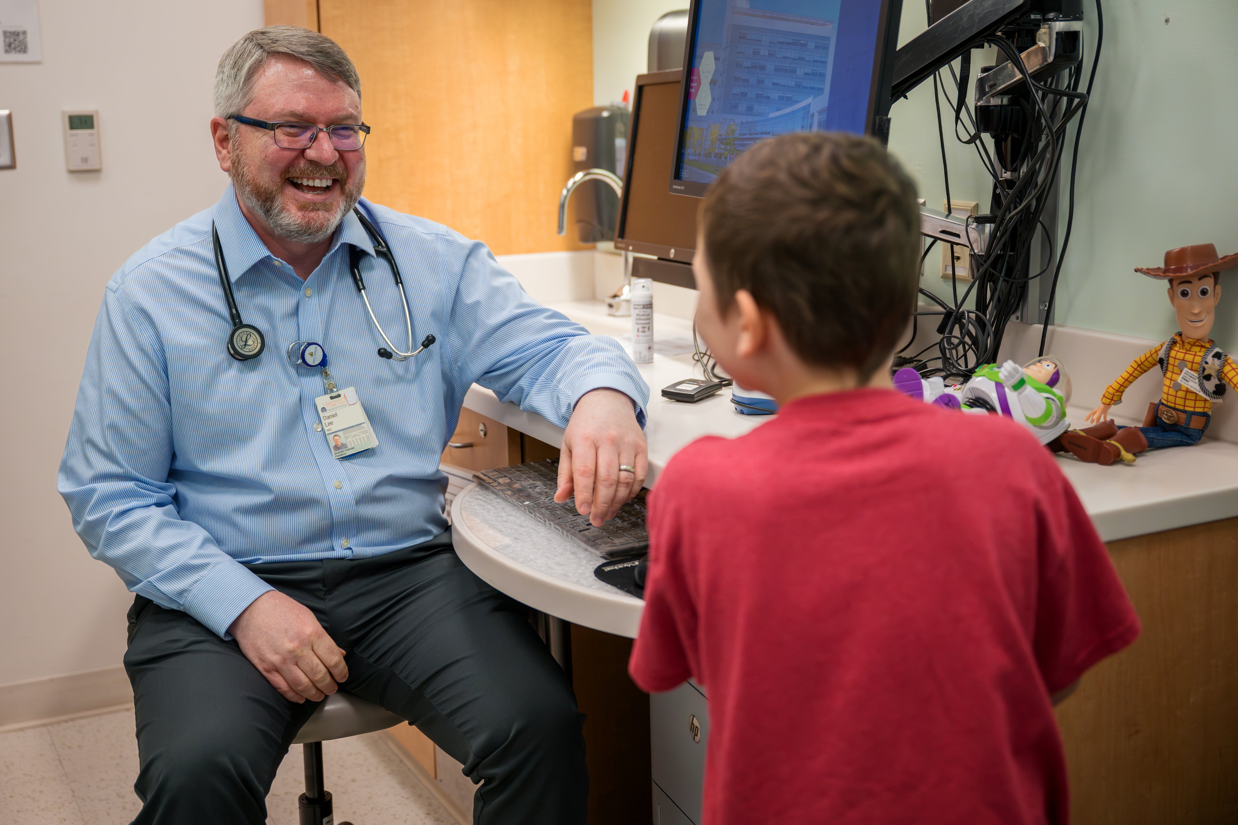Little boy in red shirt at a follow up appointment with pediatric oncologist Dr. Lee, who is smiling broadly