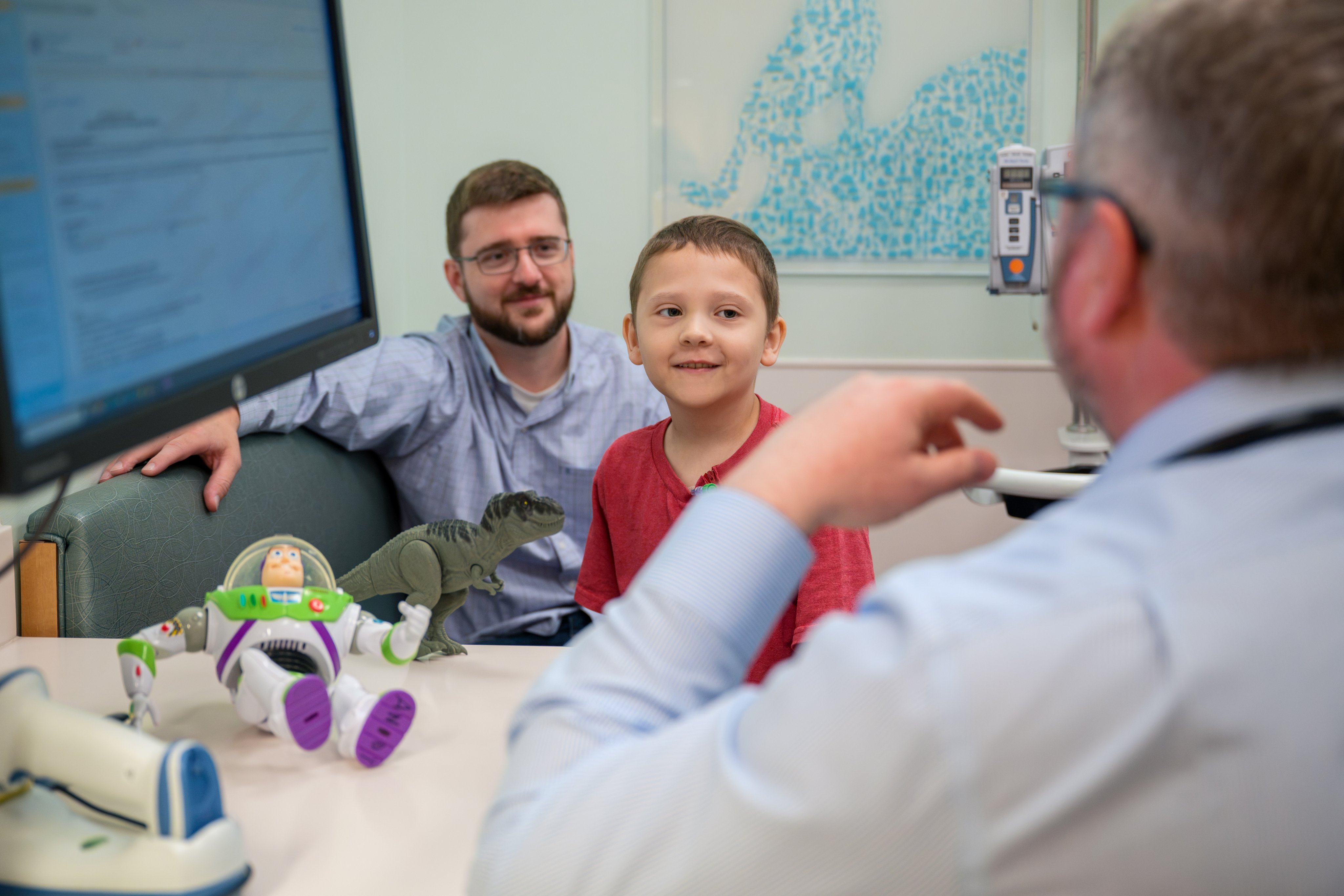 Young boy who has survived cancer meets with oncologist with smiling dad in background