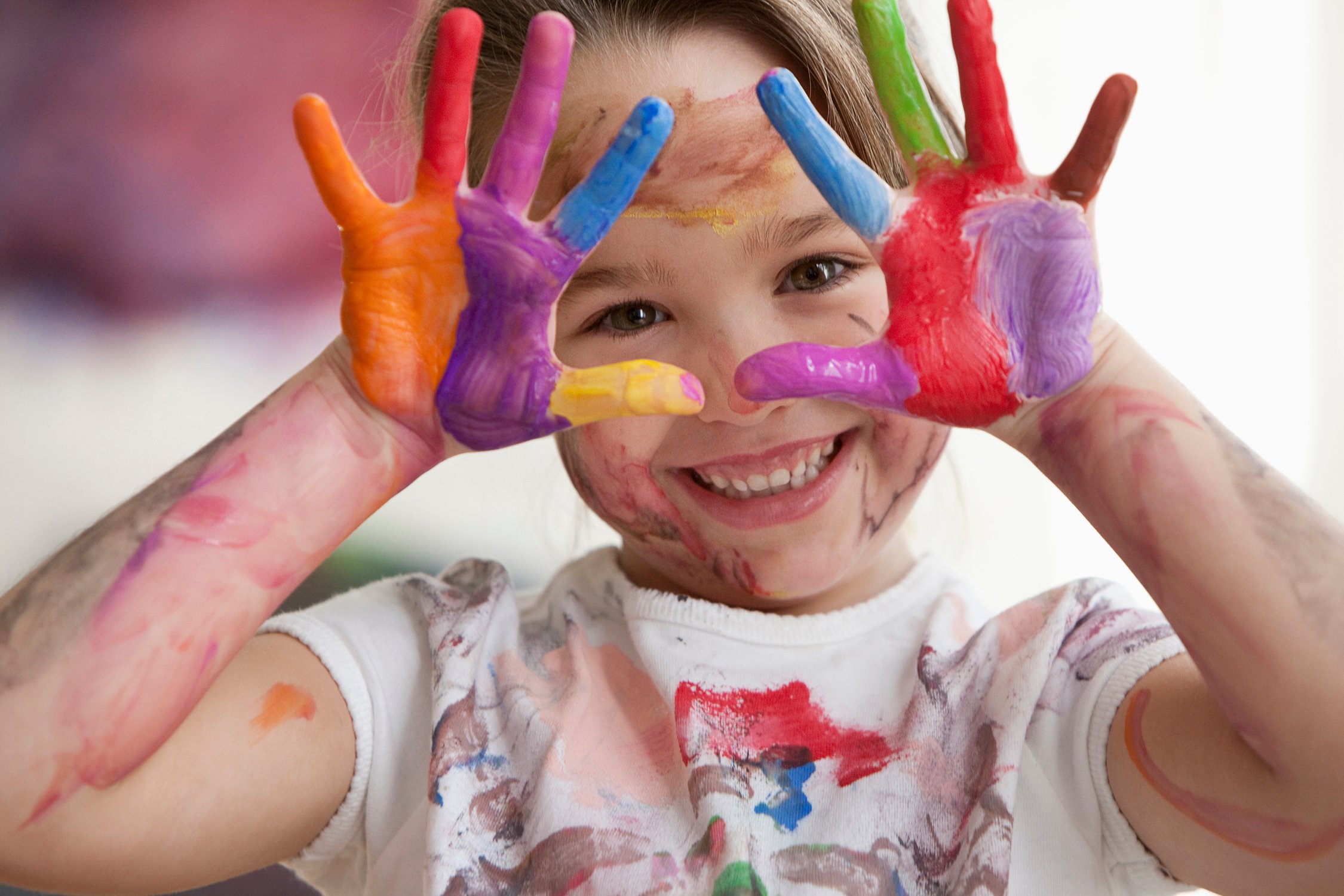 child with bright paint colors on hands smiling