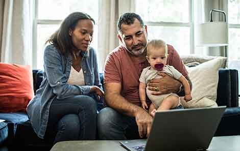Couple holds baby and looks at computer