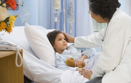 Doctor speaks to child patient in hospital bed with hand resting on her head