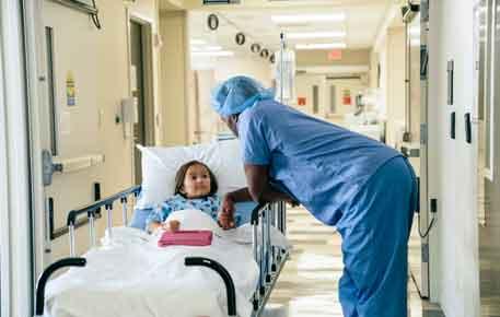 Surgeon in blue scrubs comforts child on hospital bed