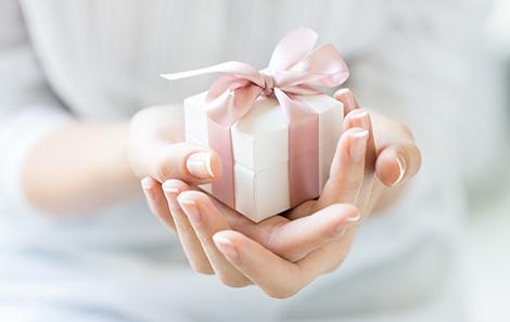 A pair of hands holding a small gift: a white box with a pink ribbon in a bow