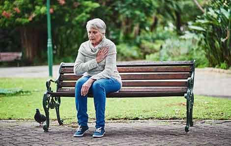 A woman sitting on a park bench with her hand on her chest