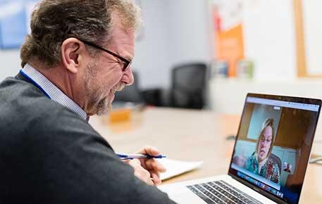 Man in suit talks to another person using a computer