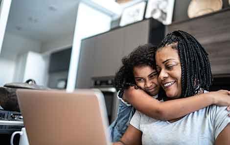 A child hugging their mother who is looking at a laptop screen.