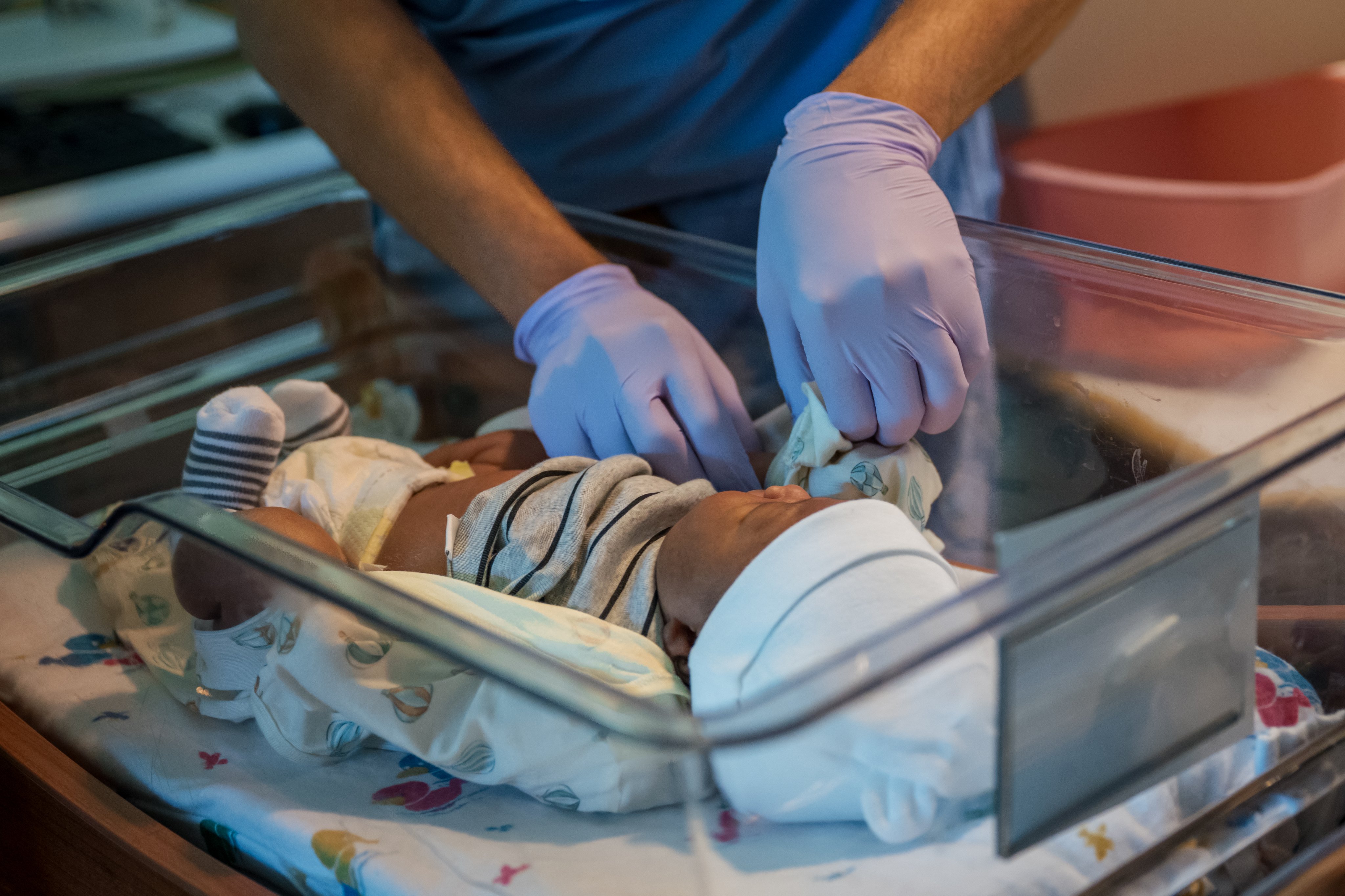 Nurse gently swaddles baby in clear bassinet