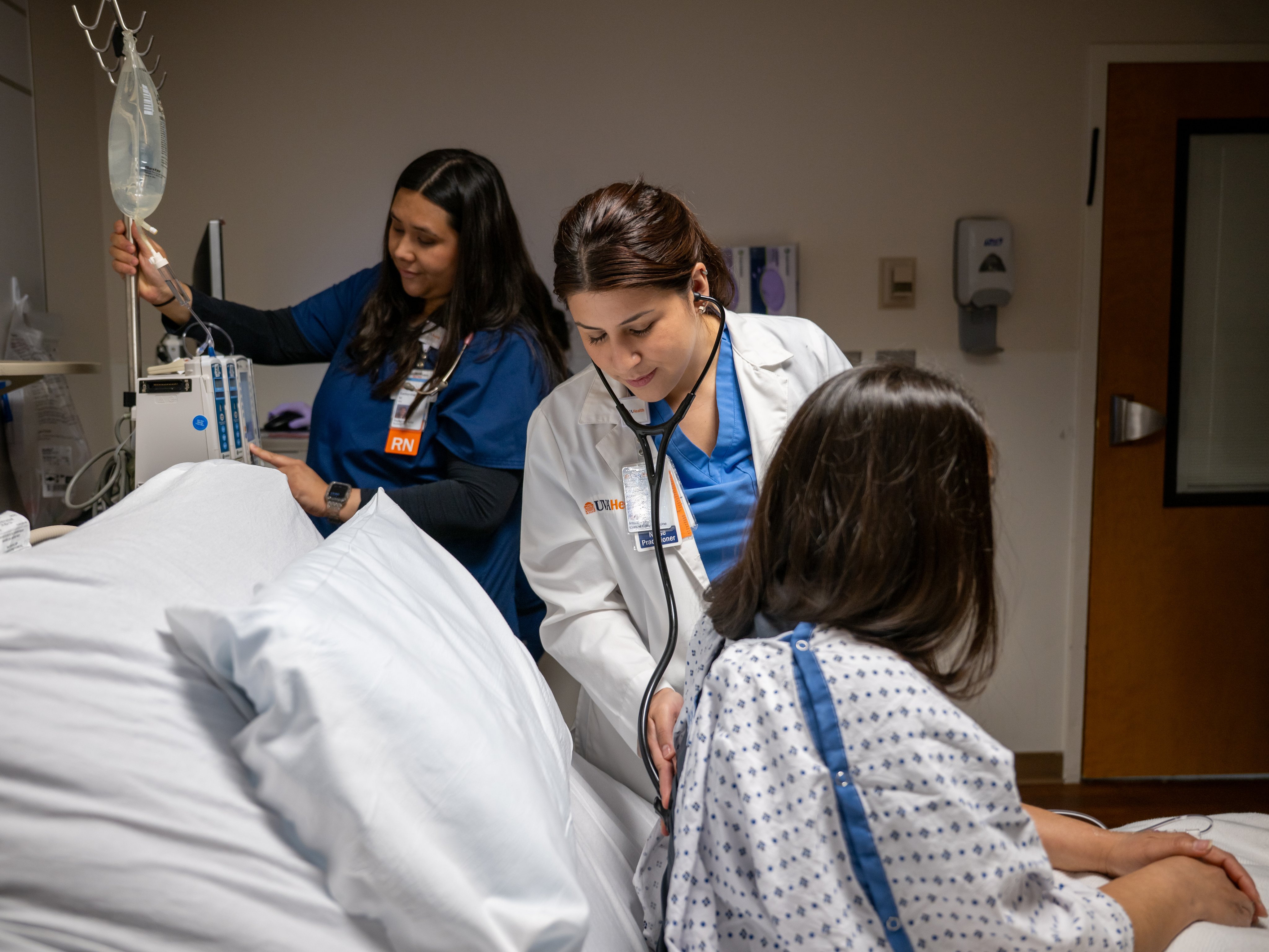 A patient sitting in a bed being attended to by two healthcare providers