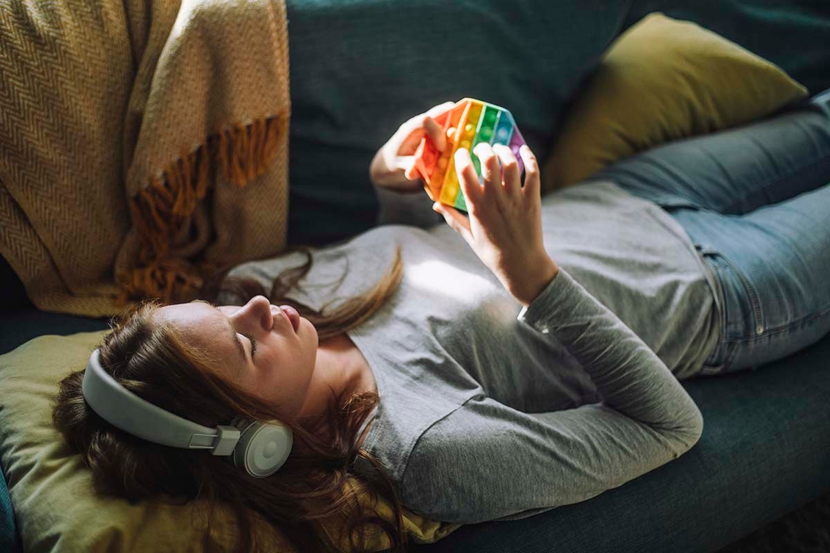 Teen girl listens to music while playing with popit fidget toy