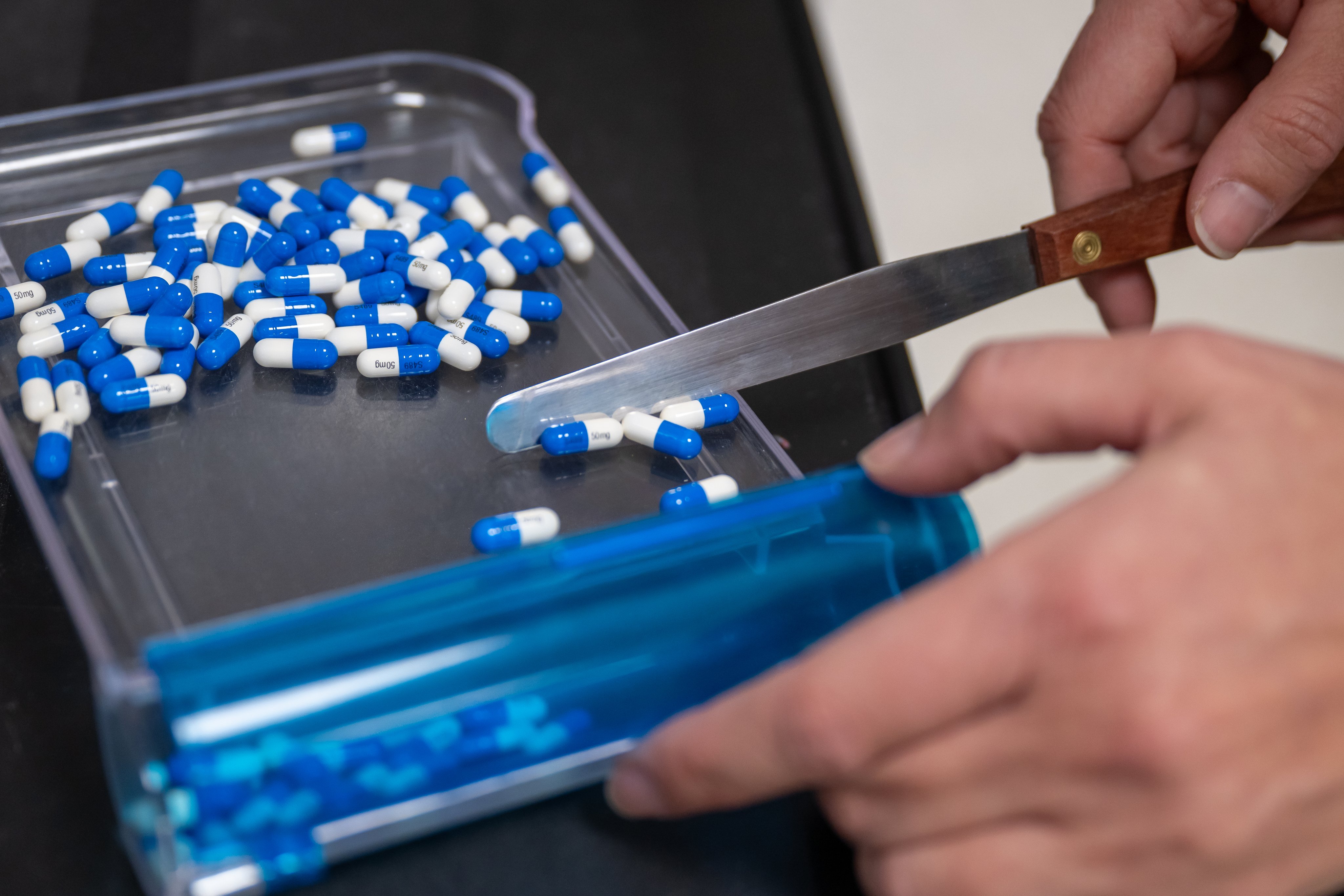 Pharmacist counts out blue and white pills for dispensing 