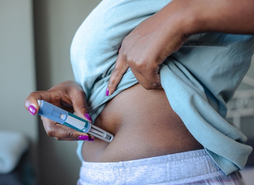 A person holding a GLP-1 injector to the skin of their abdomen