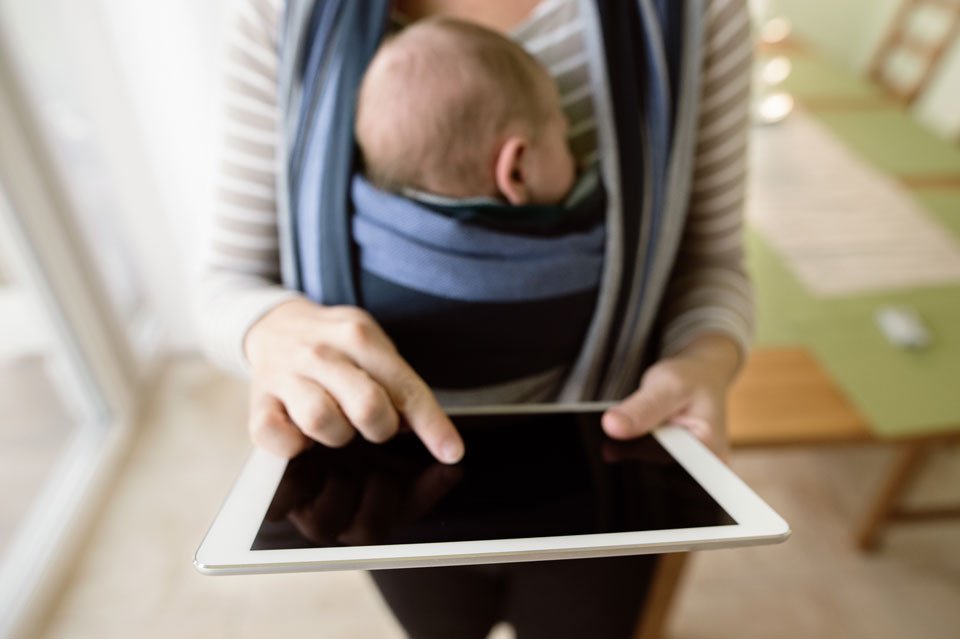 Mom with baby in carrier uses ipad