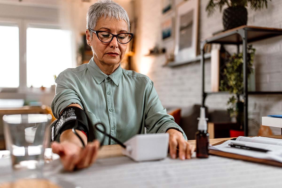 An older person sitting with a cuff on their arm and taking their blood pressure at home.