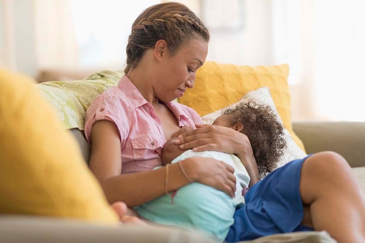 Mom smiles while breastfeeding her baby on the couch