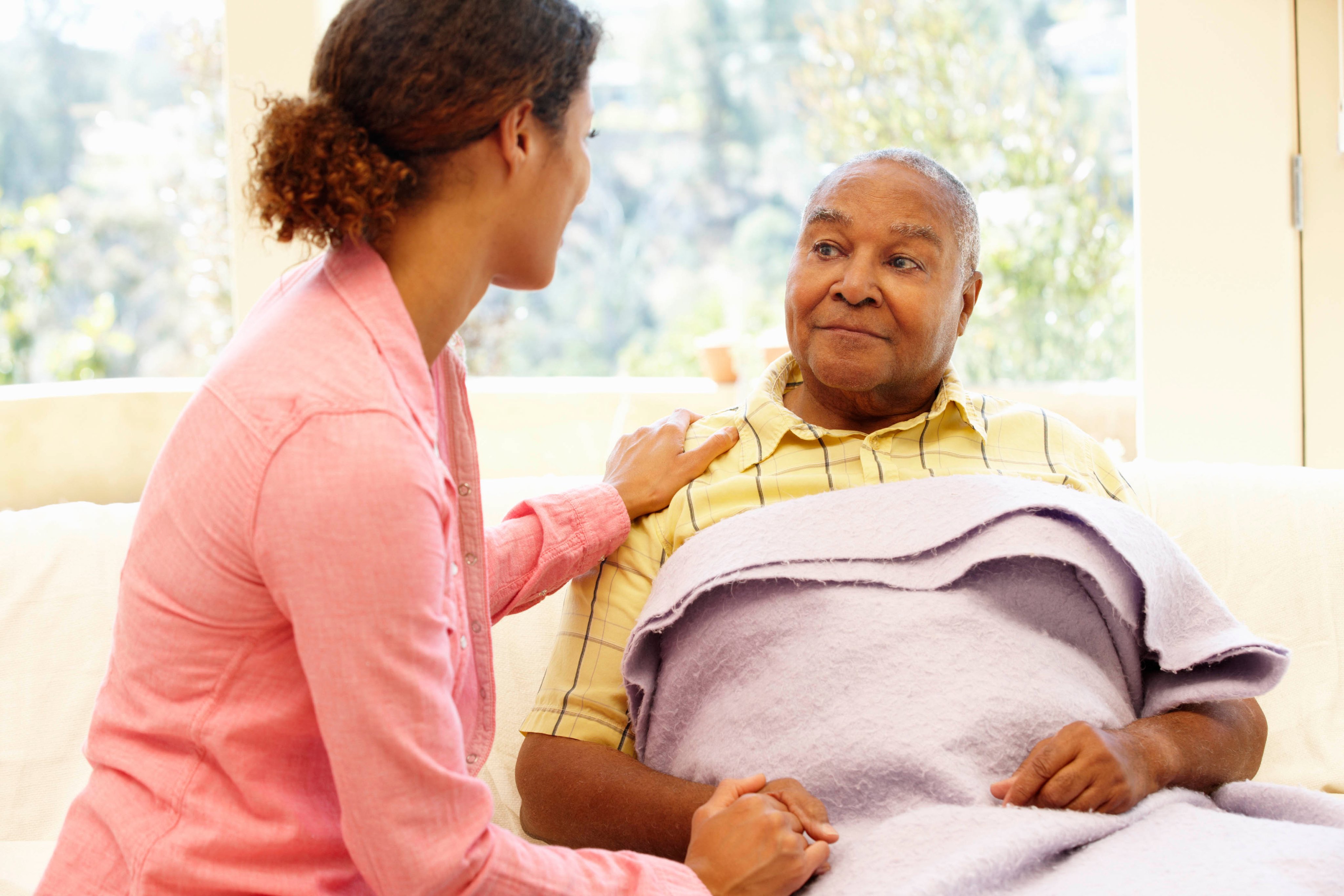 A woman touching the shoulder of a man who has a blanket on them