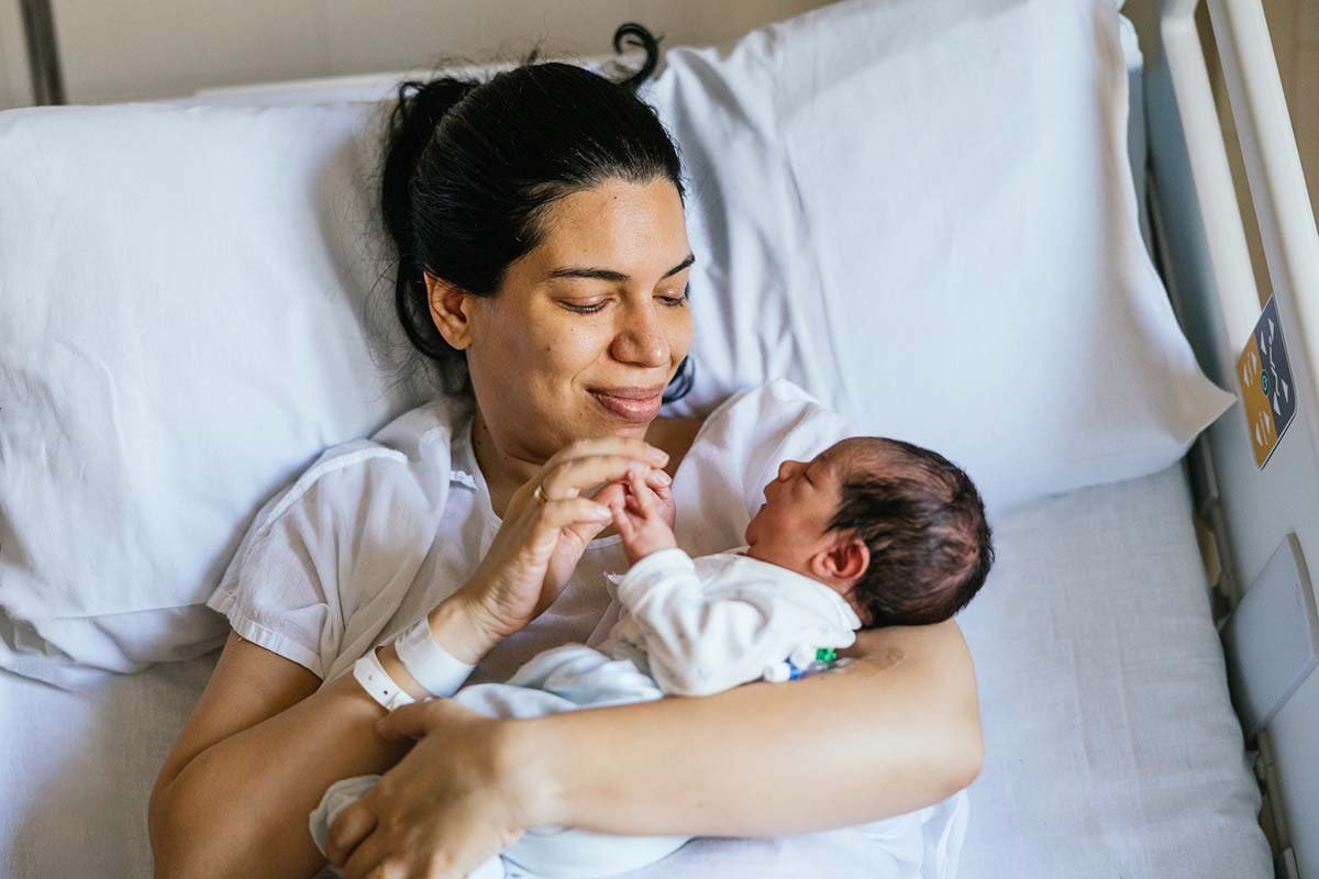 Mom holds newborn while laying in hospital bed 