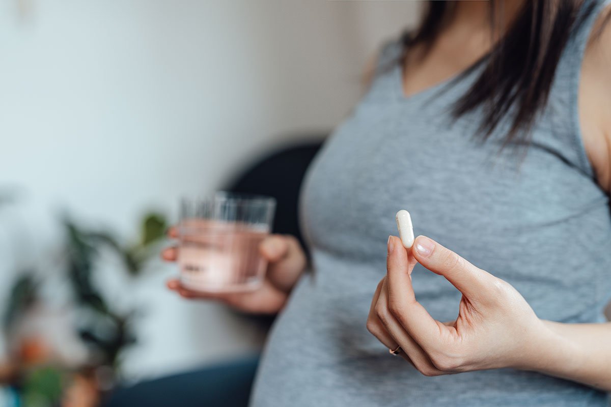 Woman holds prenatal vitamin and glass of water