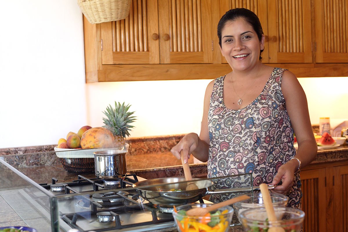 Pregnant woman cooks fresh food in kitchen and smiles at camera