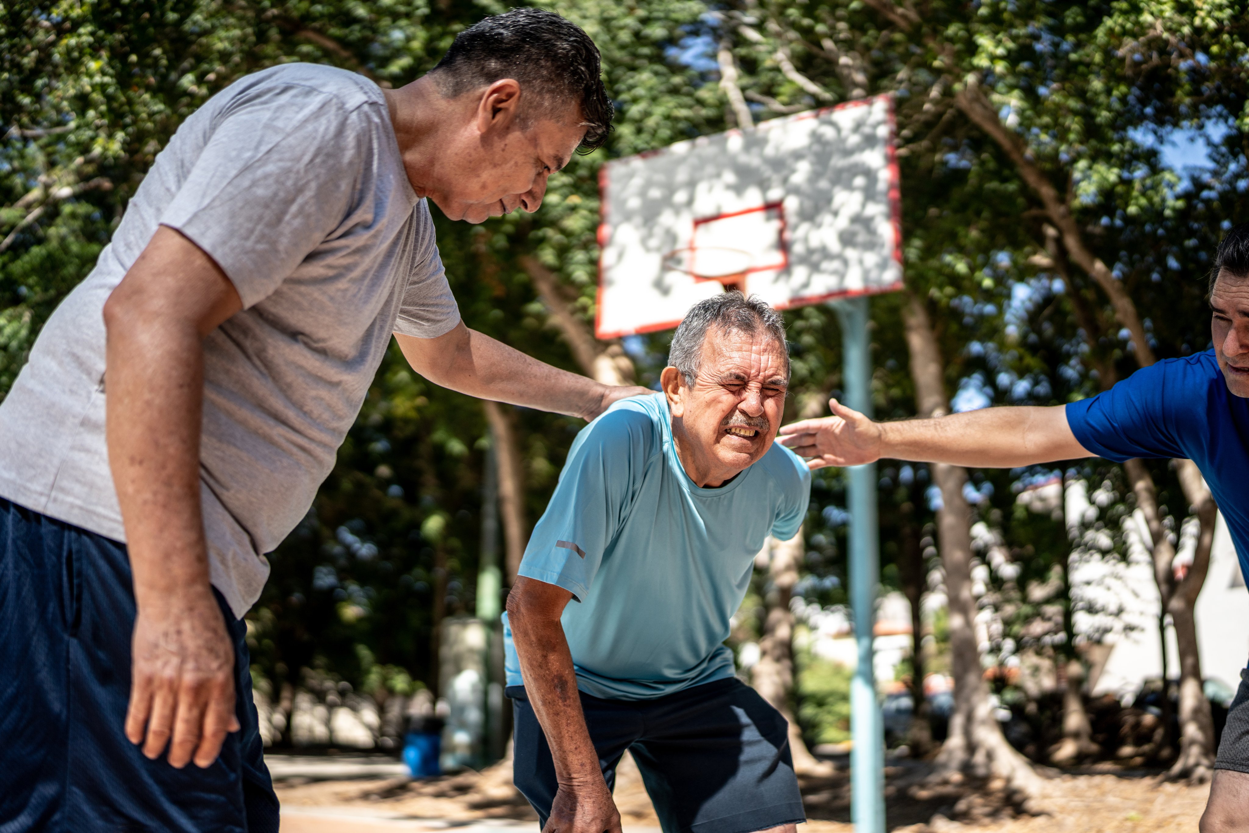An older man on a basketball court leans over in pain