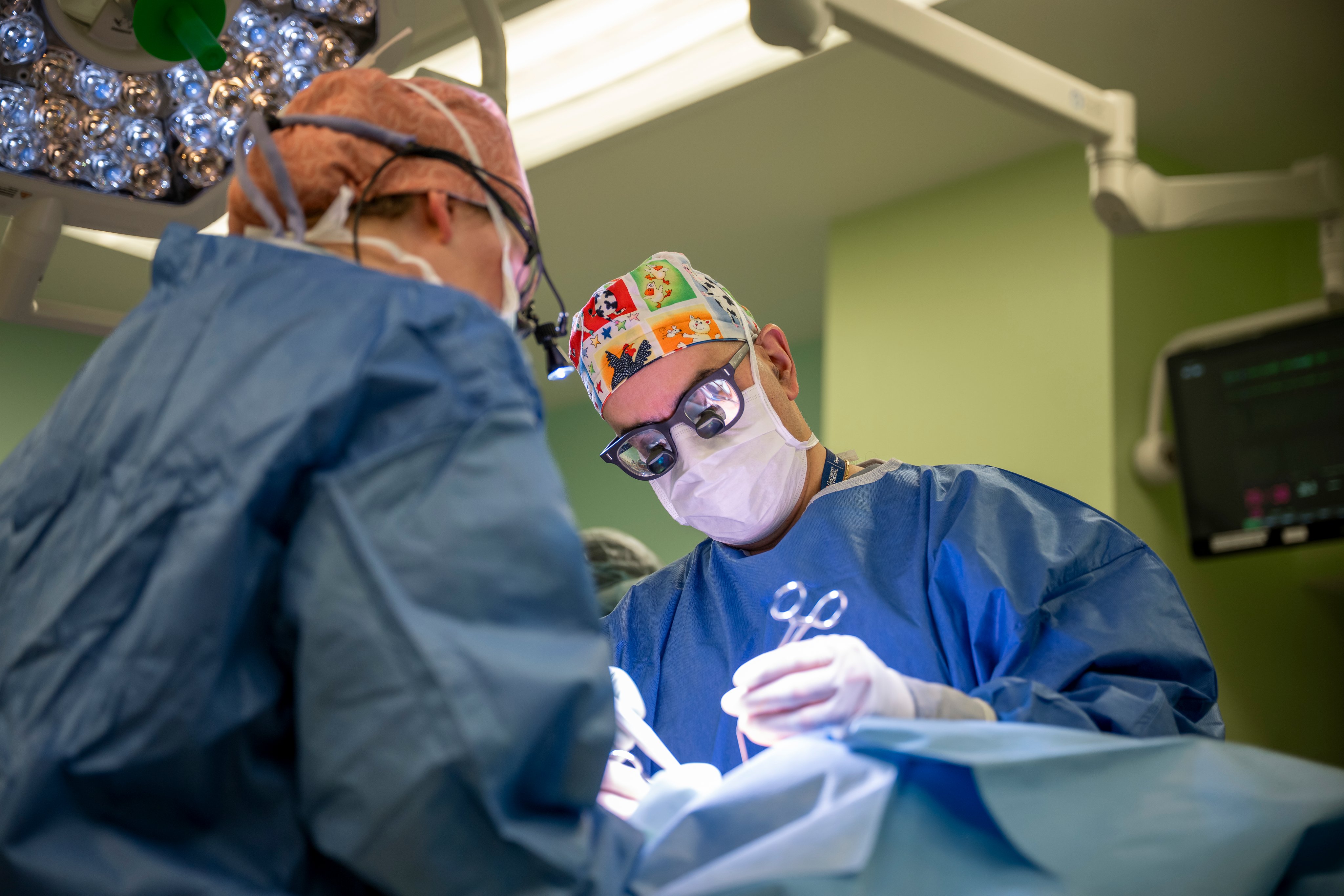 2 pediatric surgeons in an operating room suite with bright lights and protective gear