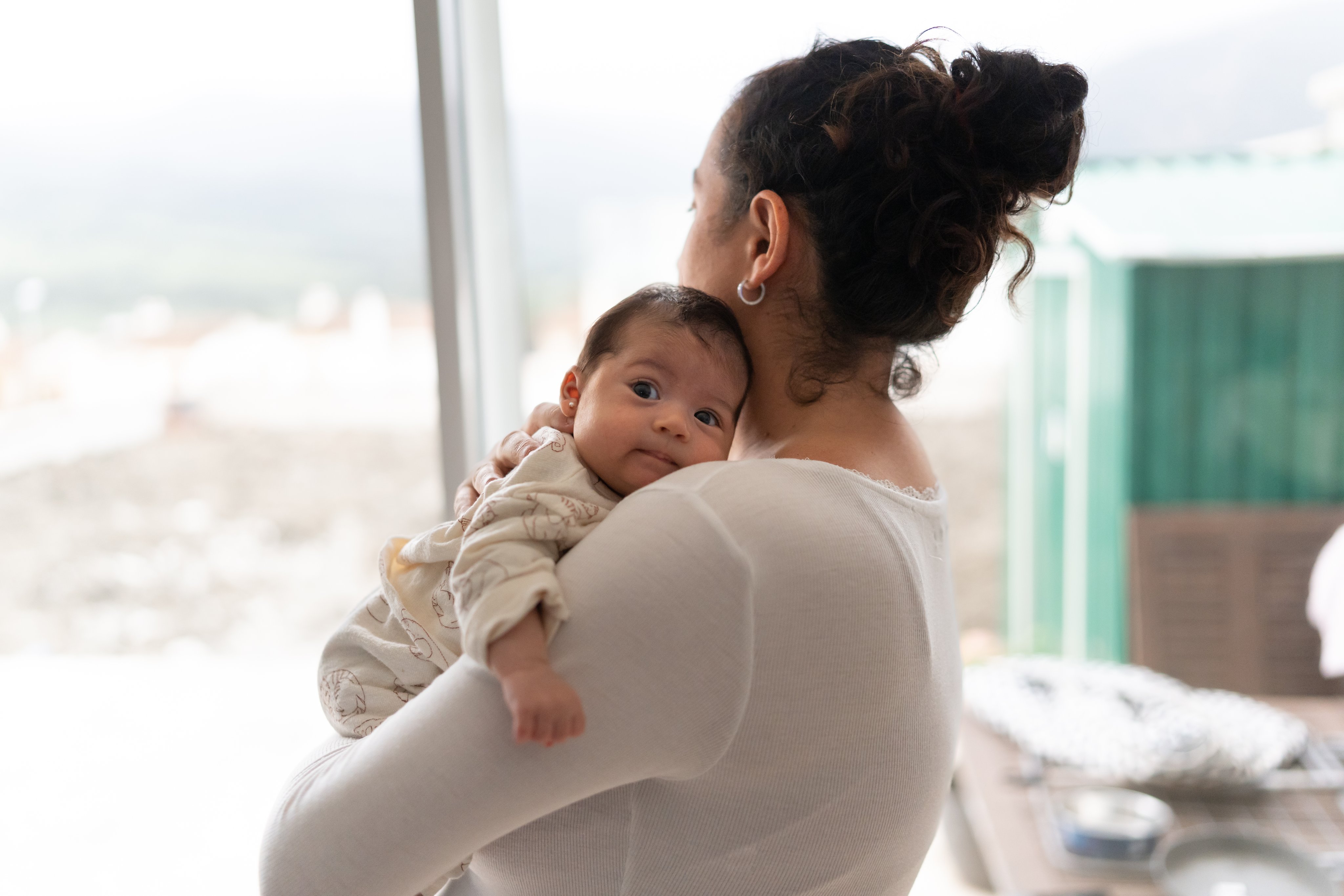 Mom wearing white holds newborn and looks out window