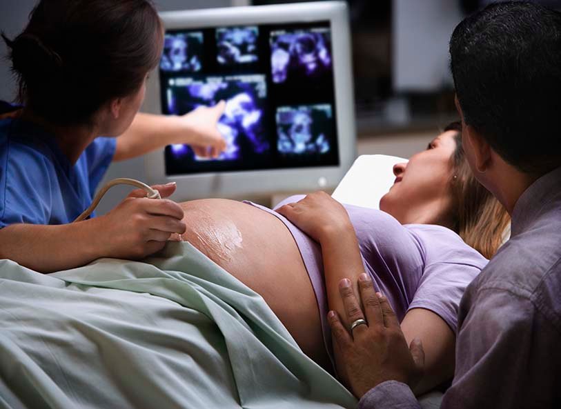 Doctor points to ultrasound while pregnant woman looks closely