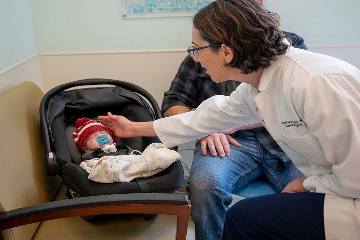 Dr. Spader in white coat reaches out to a newborn patient sleeping in a carseat