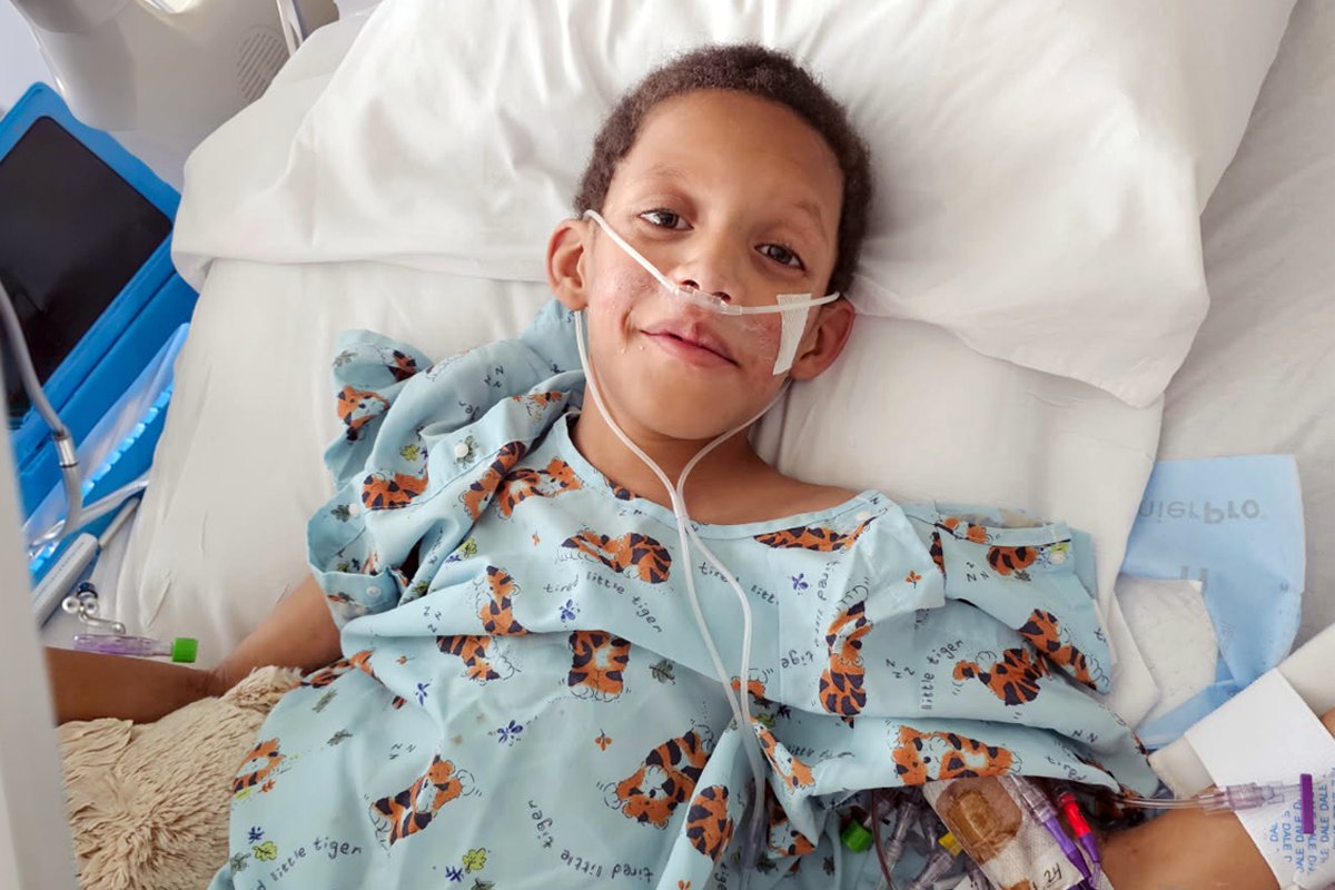 Young boy in hospital gown laying in bed with oxygen cannula, smiling after heart transplant 