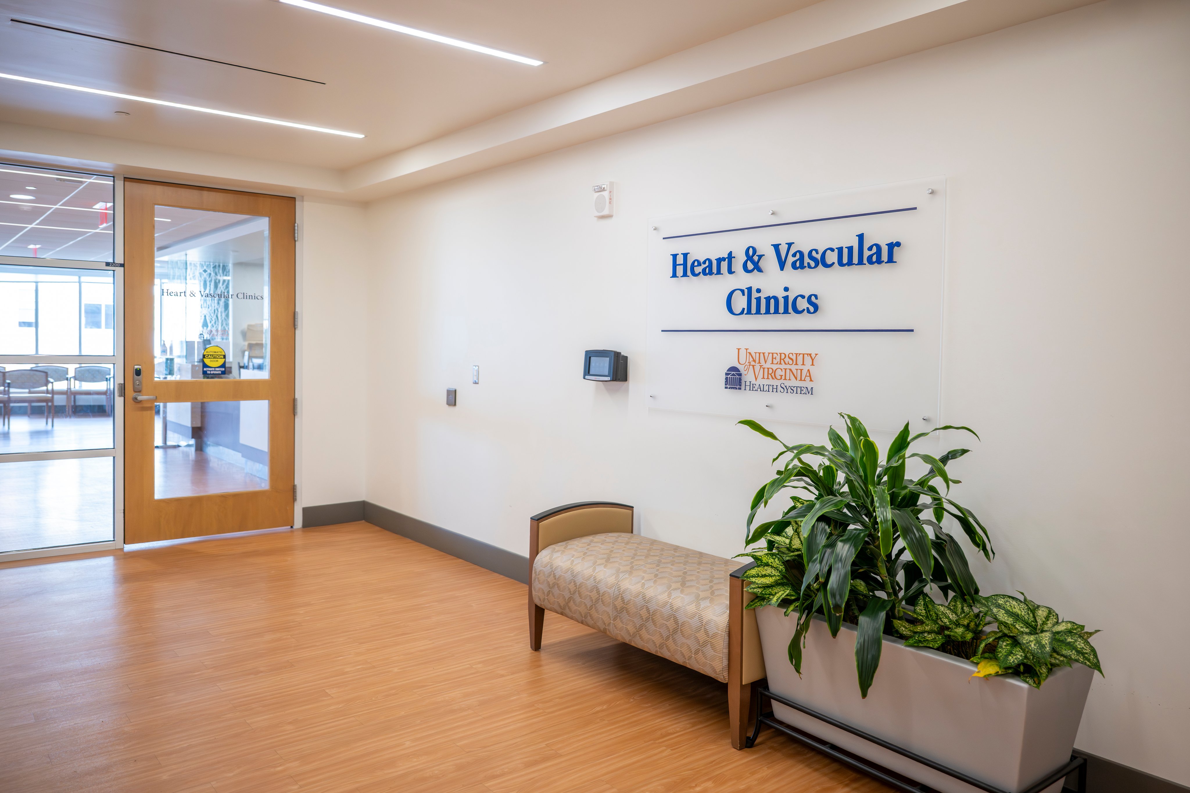 A hallway with a bench and a sign on the wall that reads "Heart and Vascular Clinics" with the UVA Health logo
