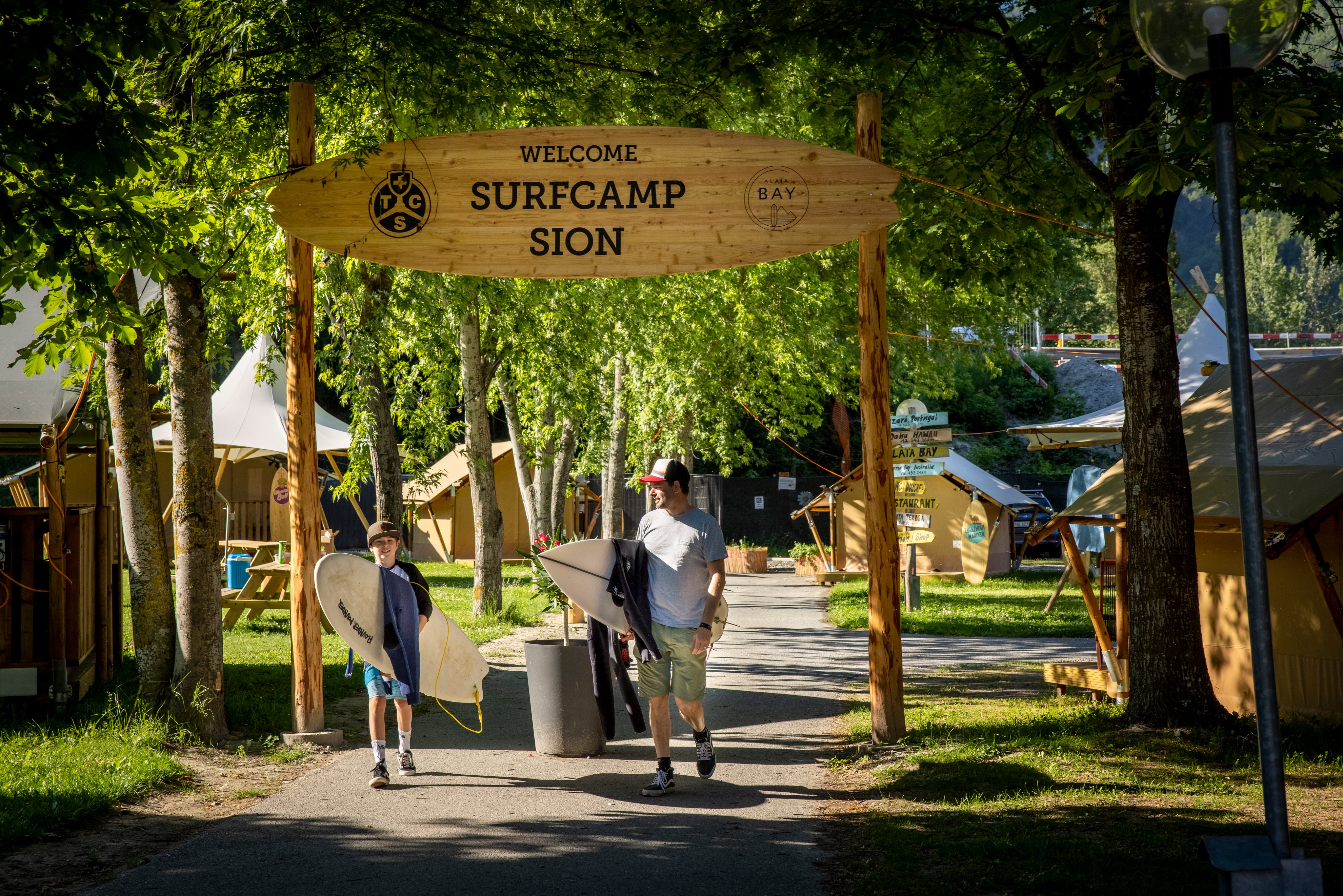 Un homme et un garçon quittent le camp de surf sur un terrain de camping avec leurs planches de surf.