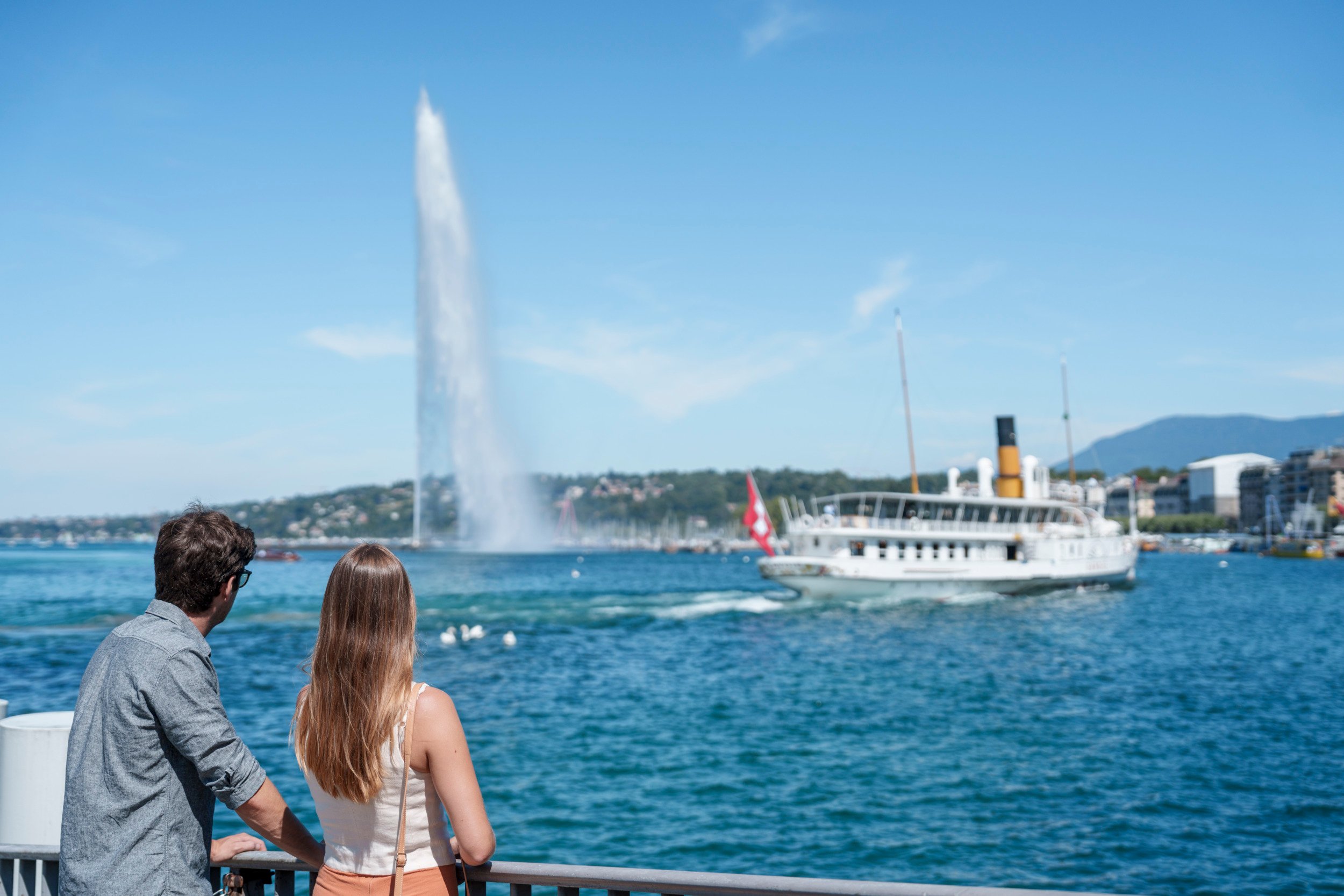 Junges Paar blickt auf eintreffendes Schiff im Hafenbecken von Genf.