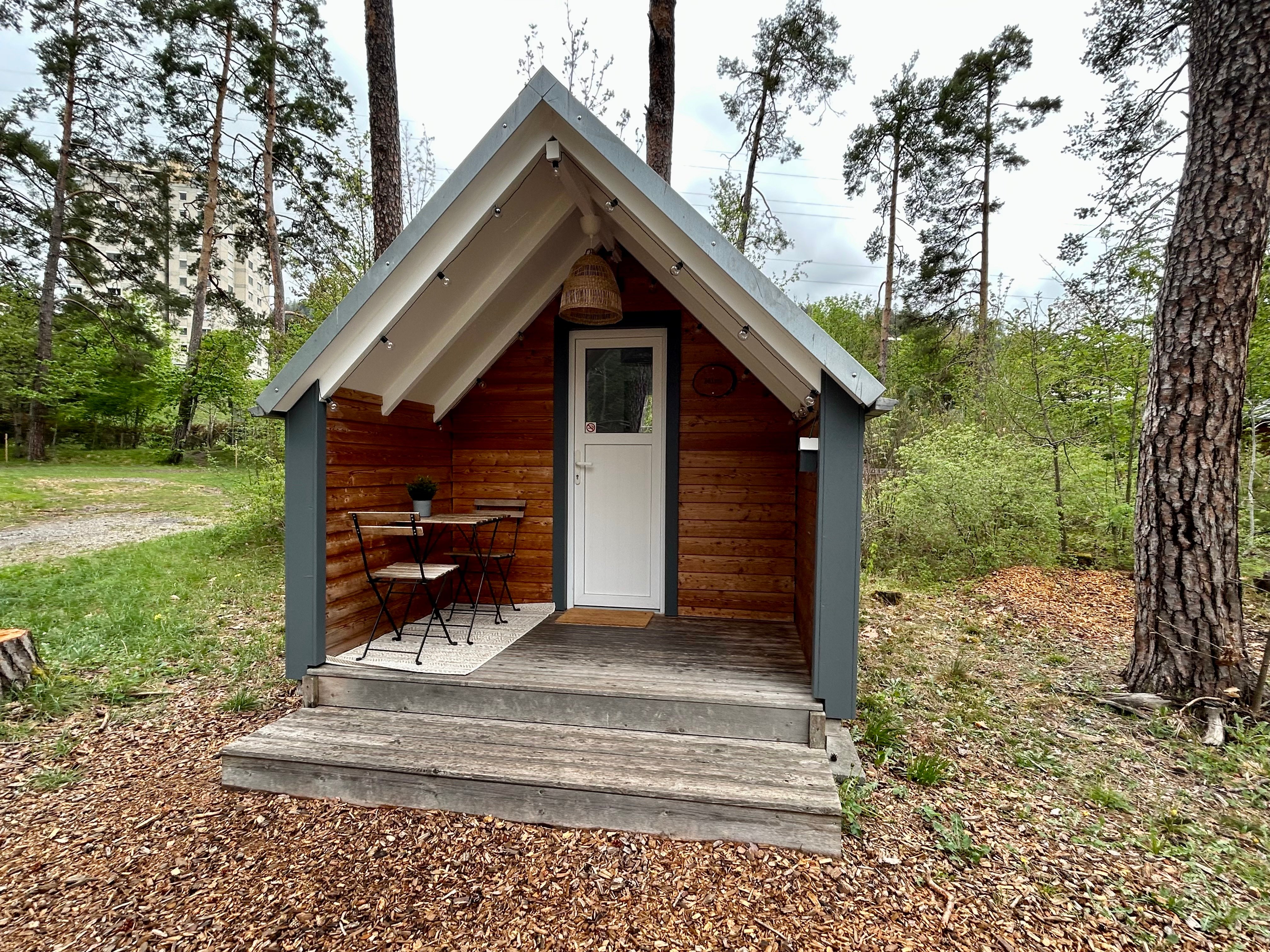 Un petit chalet sous les arbres avec une petite terrasse.