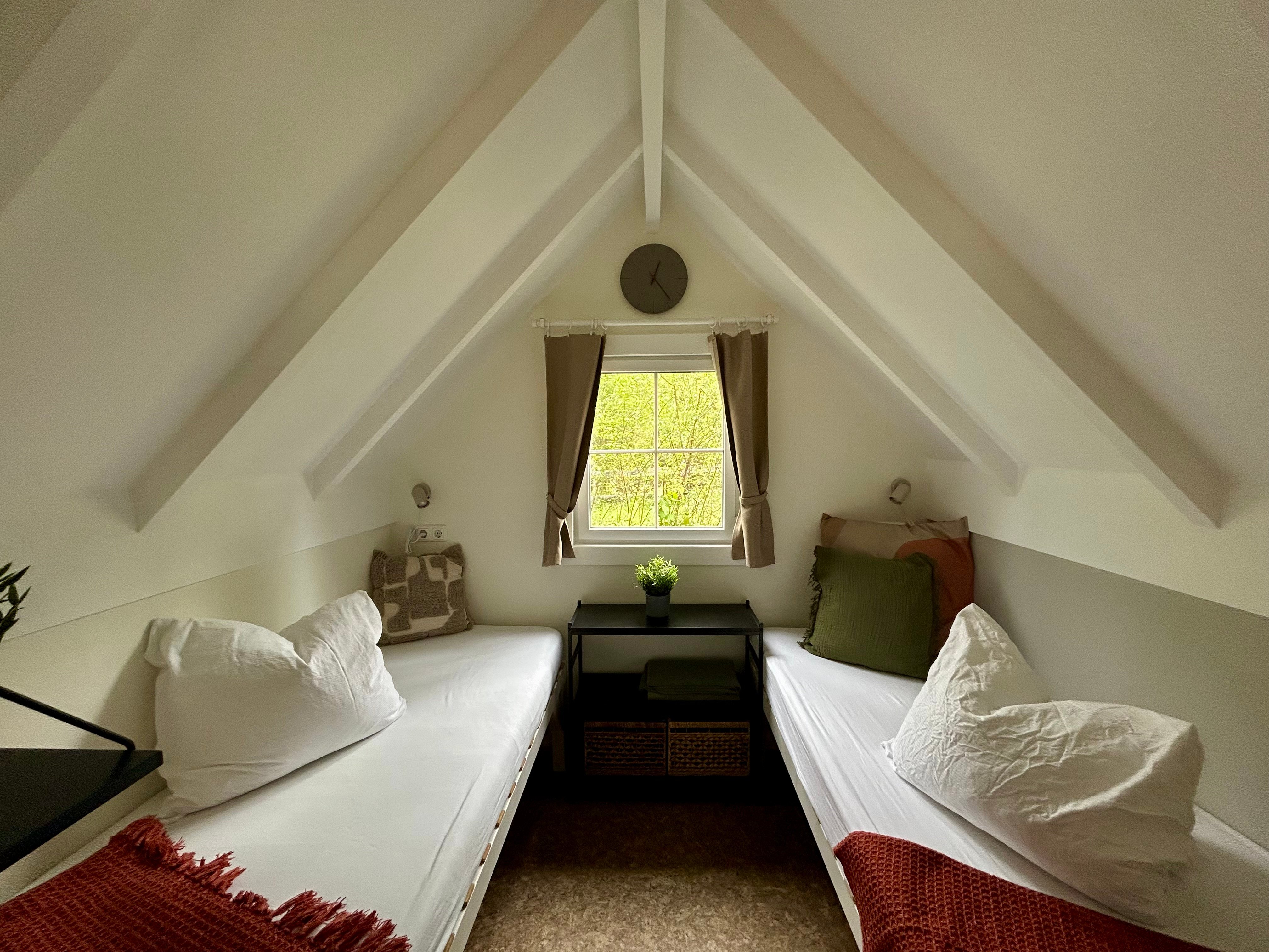 La vue intérieure du petit chalet montre deux lits simples et une fenêtre.