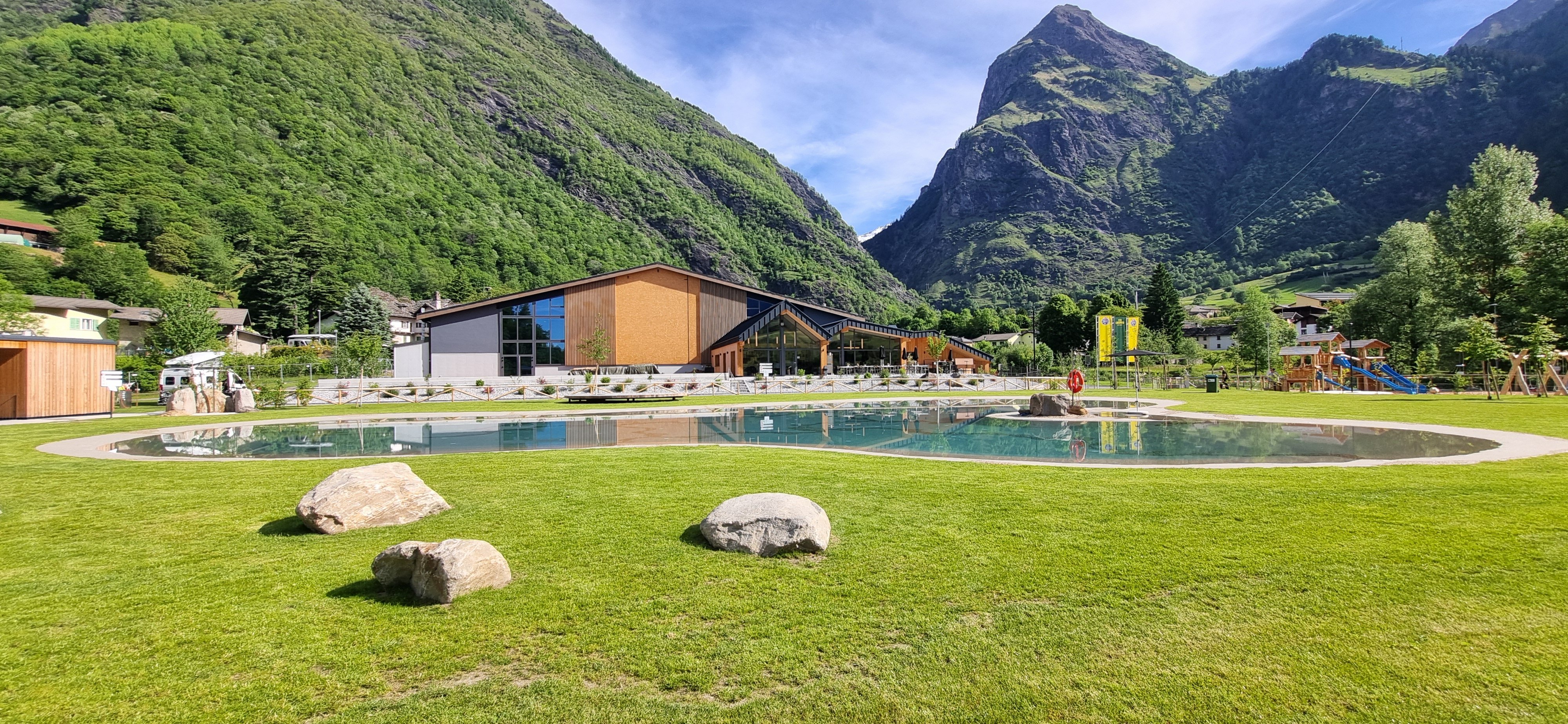 Ein grosses Gebäude mit einem Schwimmbad davor und im Hintergrund die Berge.
