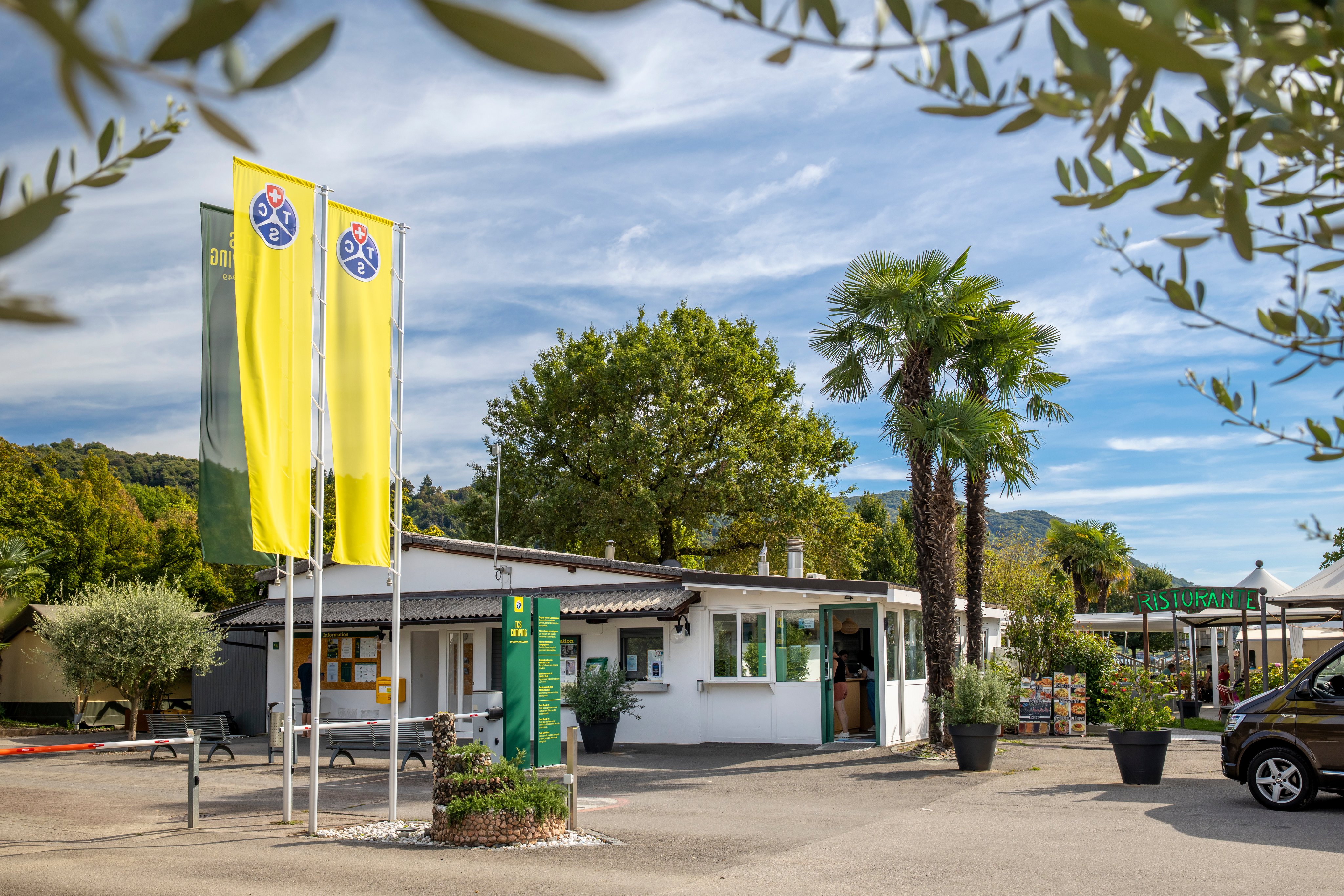 Entrée du camping TCS Lugano-Muzzano avec les drapeaux et le bâtiment de la réception.