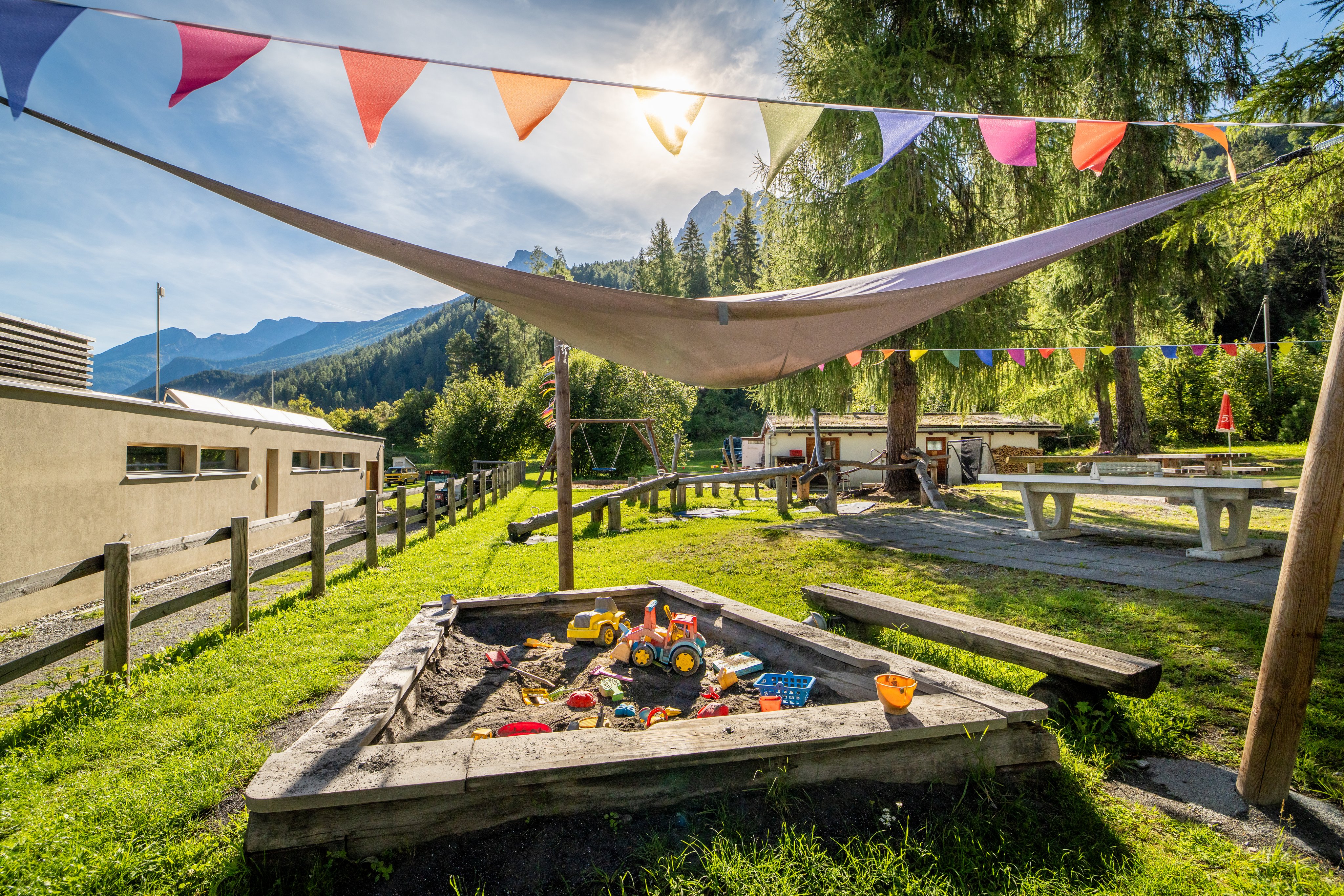 Parco giochi in un campeggio con sabbiera, altalene e tavolo da ping pong.