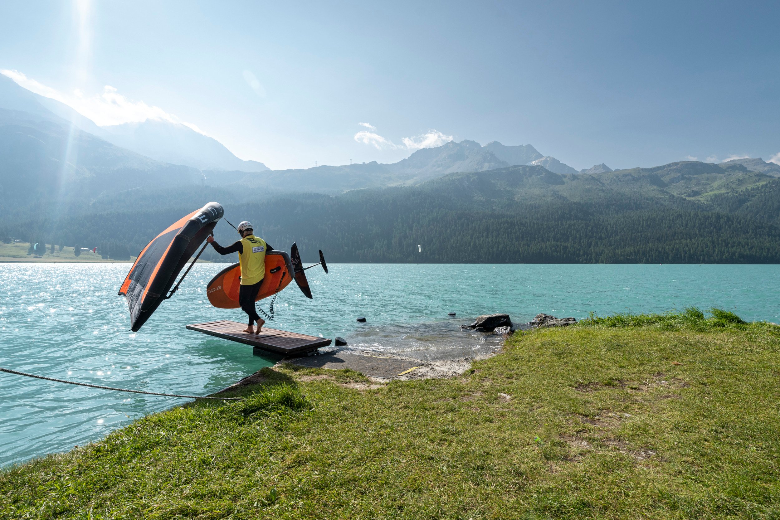 Ein Surfer läuft auf einem Steg am Silvaplanersee entlang.