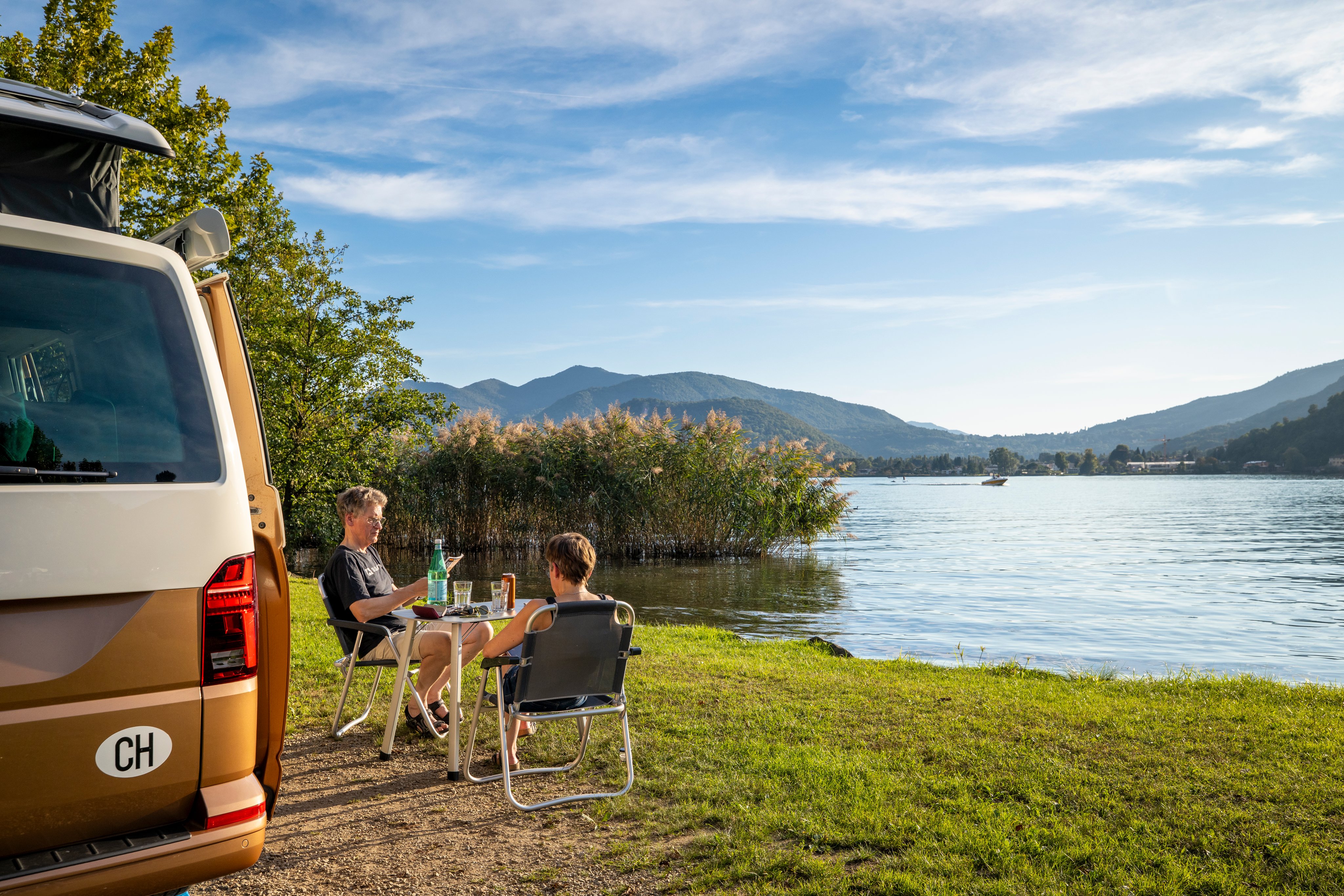 Deux personnes sont assises devant leur van avec vue sur le lac de Lugano.