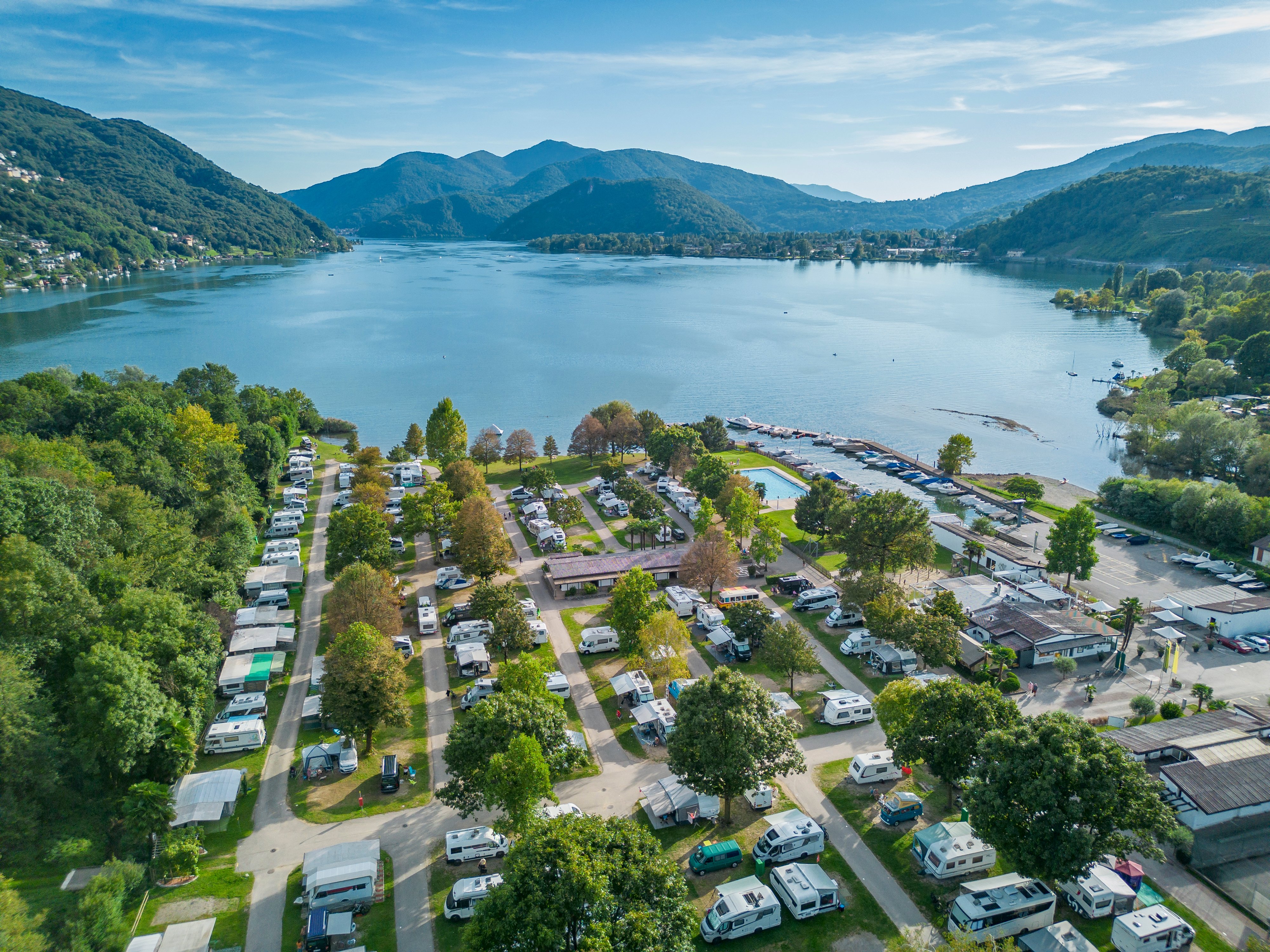 Vue aérienne du camping TCS Lugano-Muzzano avec le lac de Lugano et les montagnes en arrière-plan.