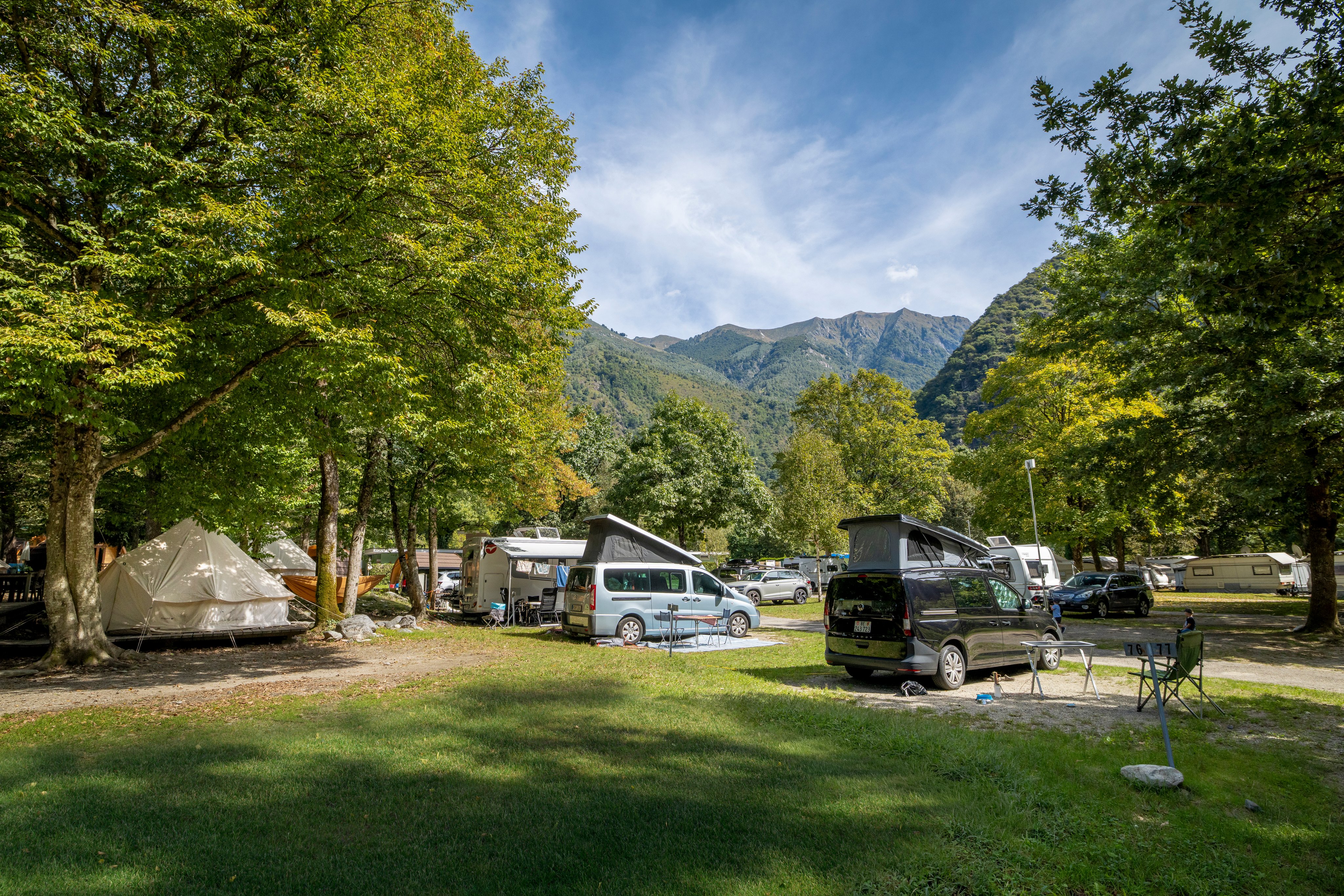 Links sind zwei Nomadenzelte und rechts davon Camping Vans vor dem Bergpanorama auf dem TCS Campingplatz Gordevio.