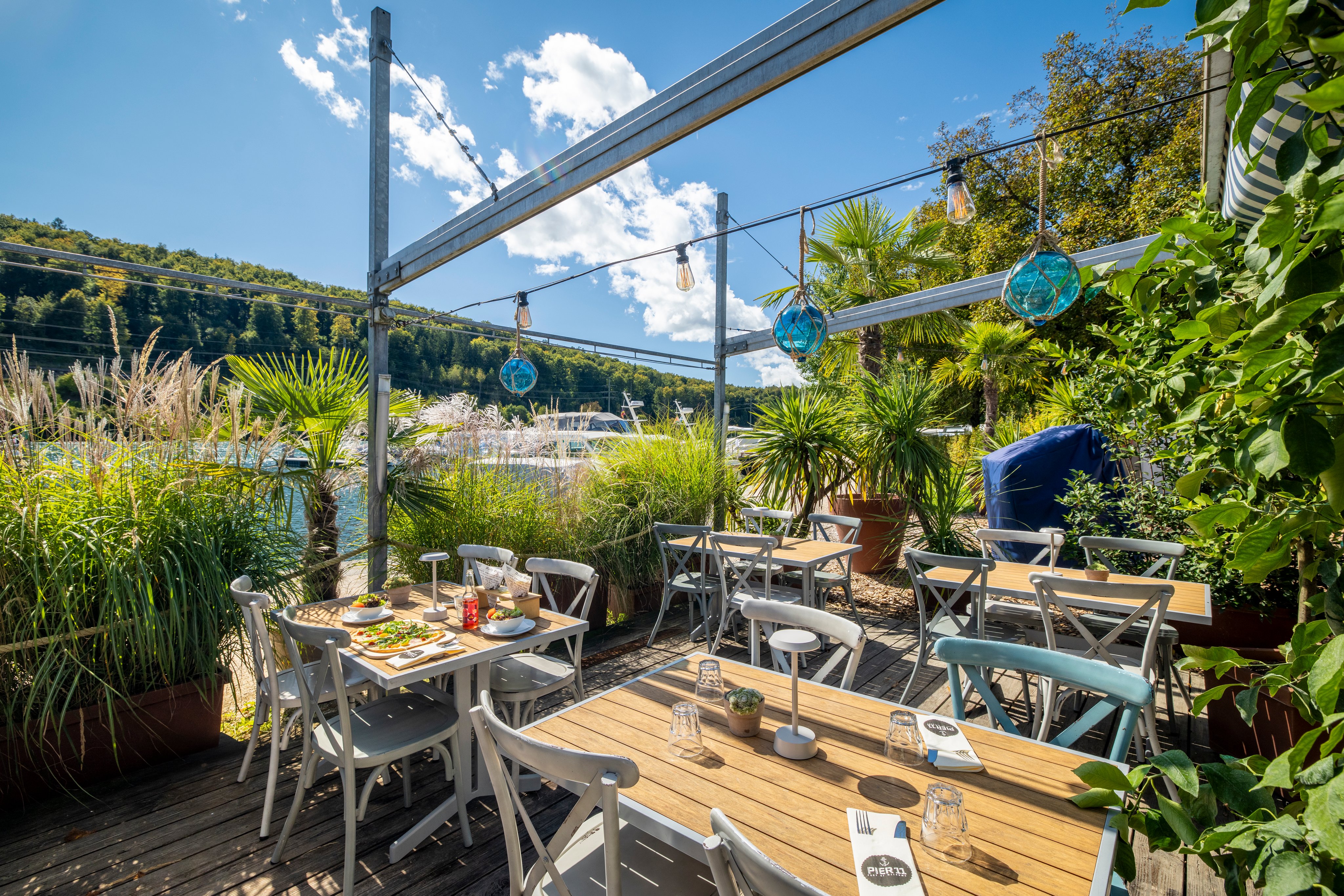 Ein Restaurant mit Aussenbereich direkt an einem Fluss mit viel Grün.