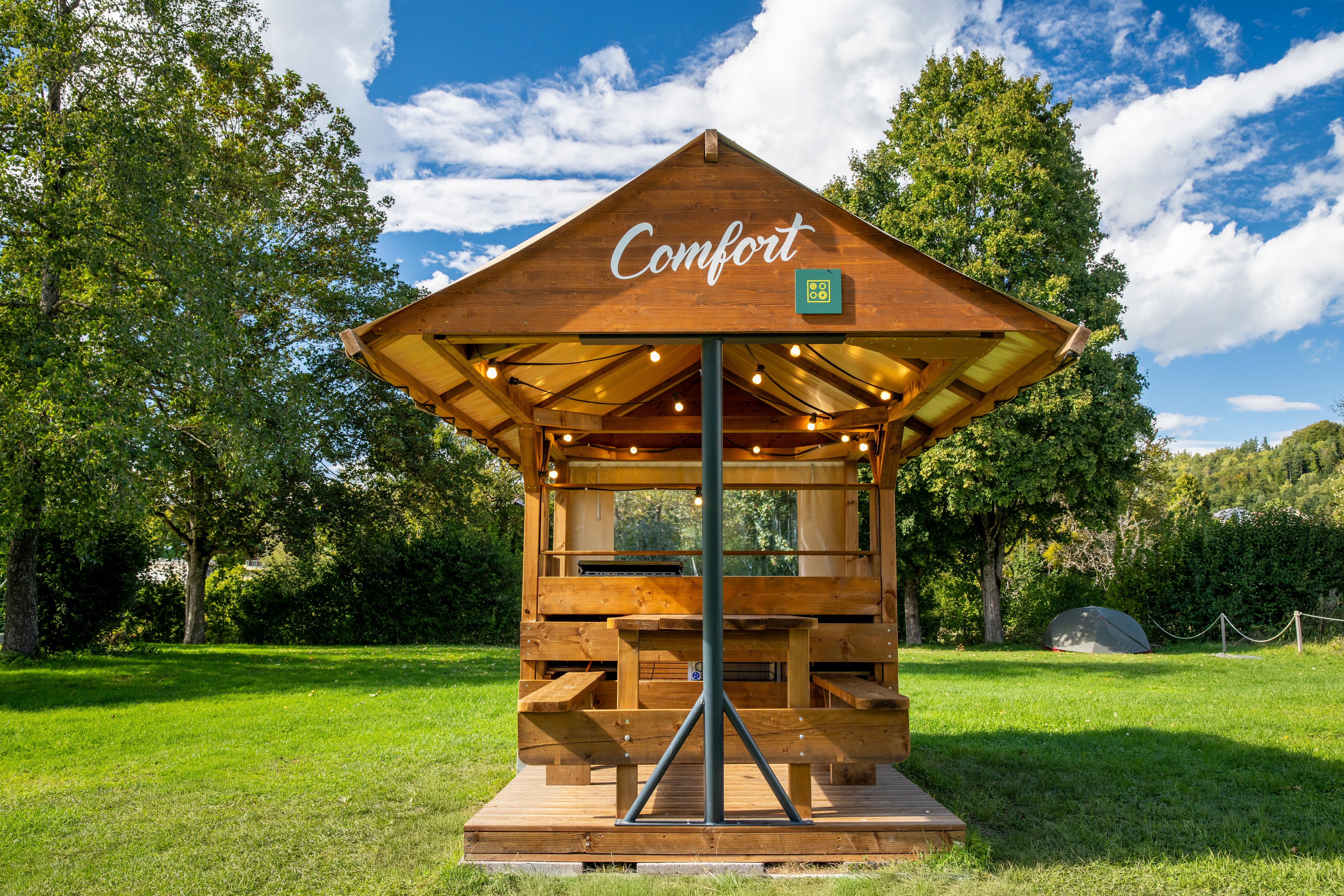 Ein Holzunterstand mit Tisch, Bank und Küche auf einem Campingplatz.