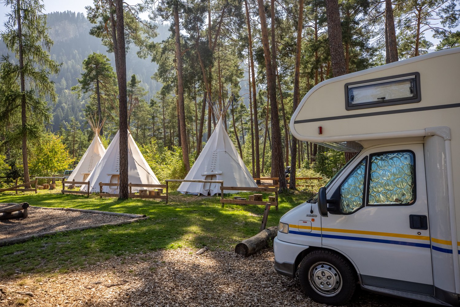 Drei Tipis und ein Camper auf einem Campingplatz unter Bäumen.