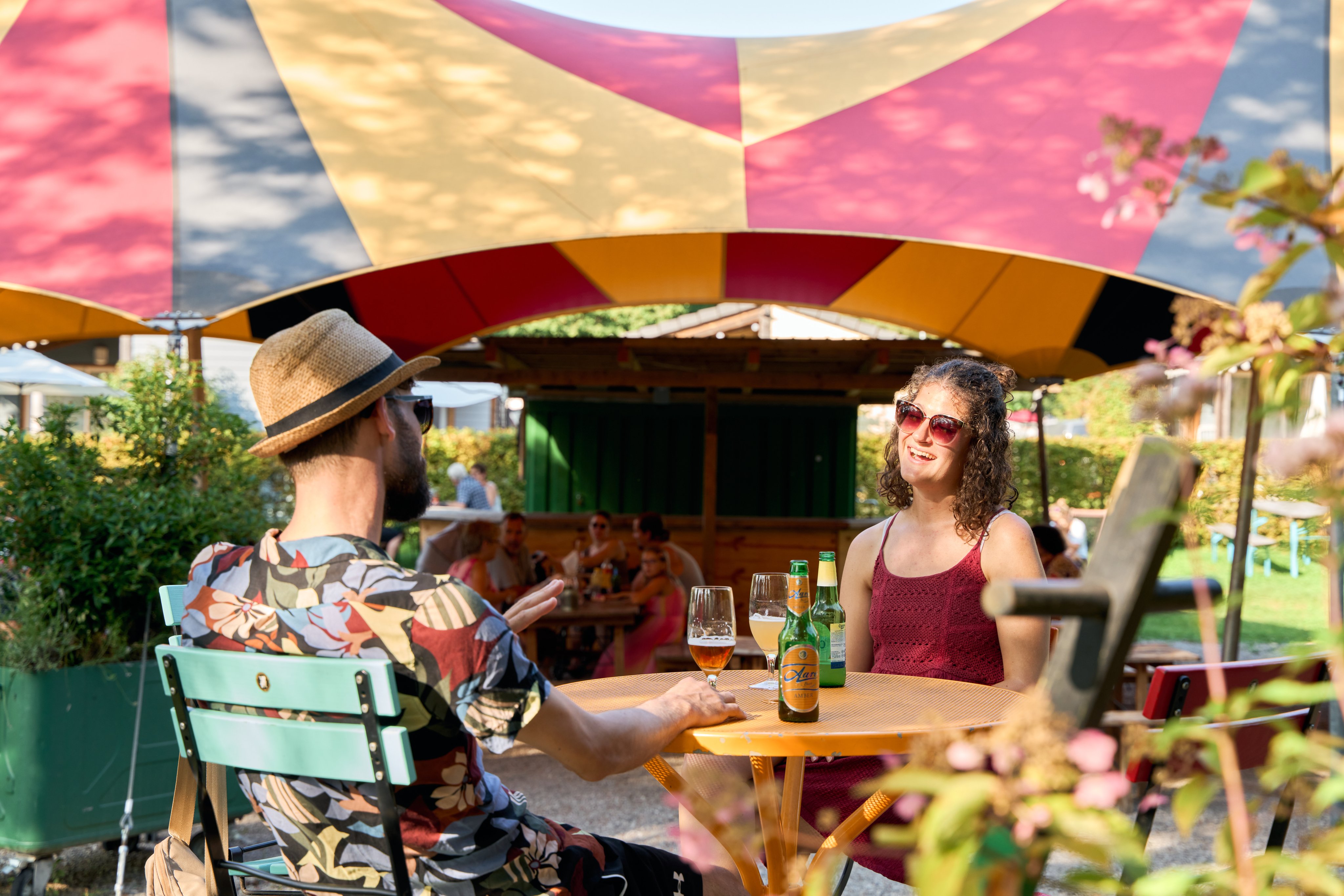 Two people sit on a terrace under a circus tent and drink an aperitif.