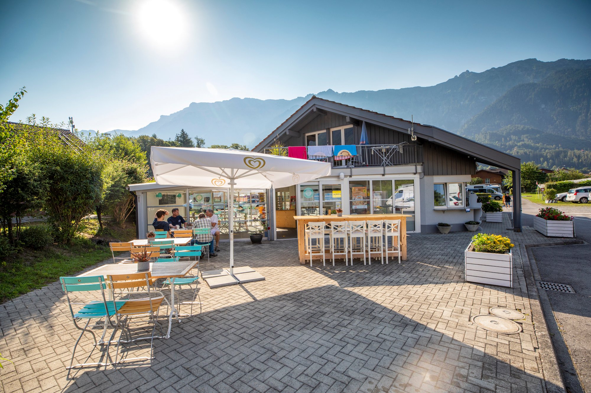 Une terrasse avec des tables, des chaises et quatre personnes sur un camping.