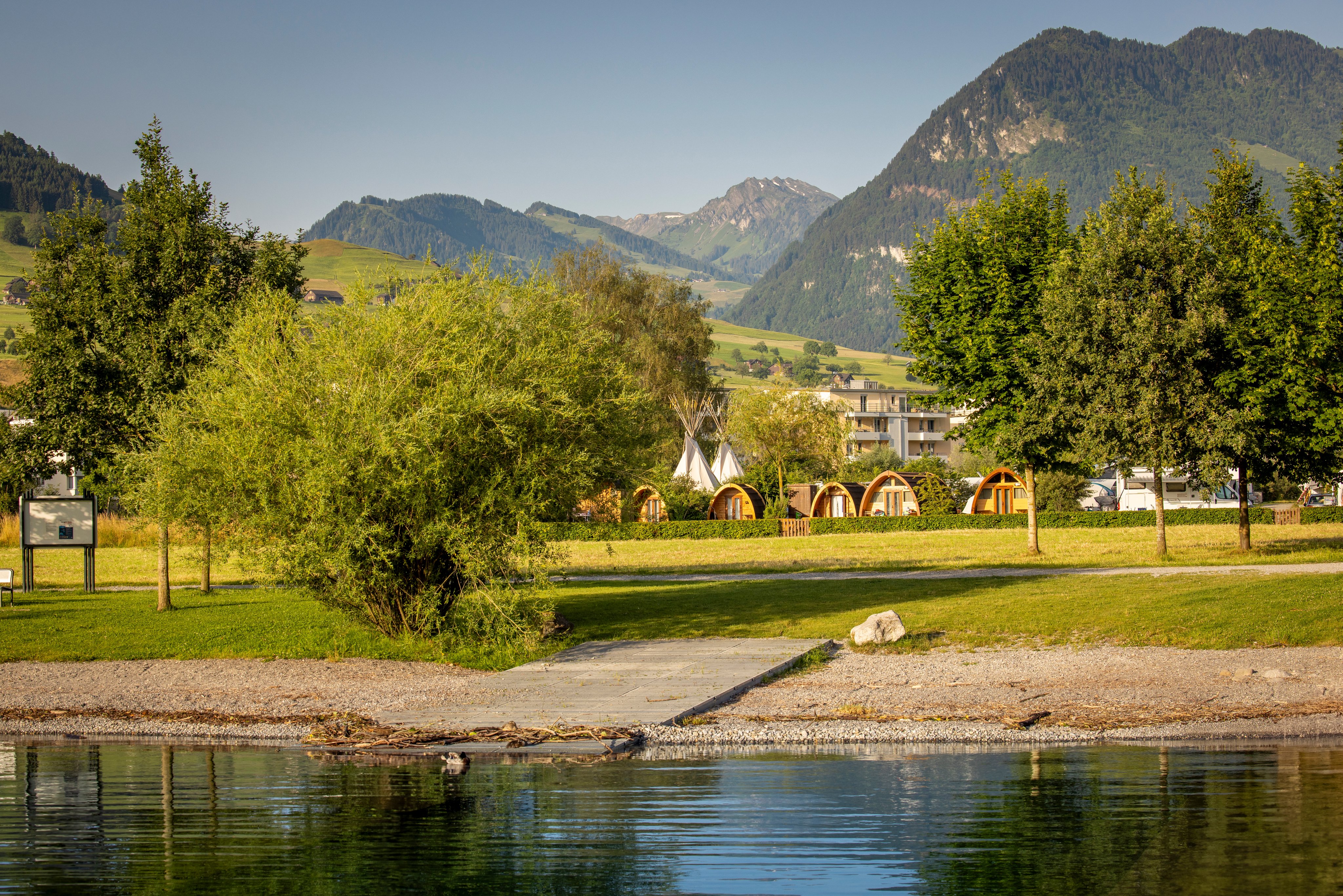 The shore of a lake, with a campsite in the background.