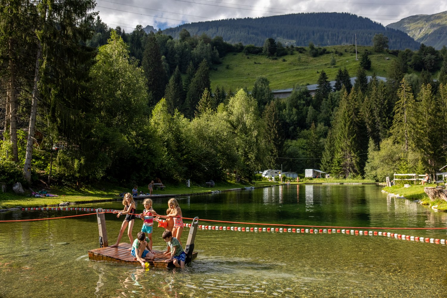 Children on the raft on the natural swimming lake at TCS Camping Disentis.