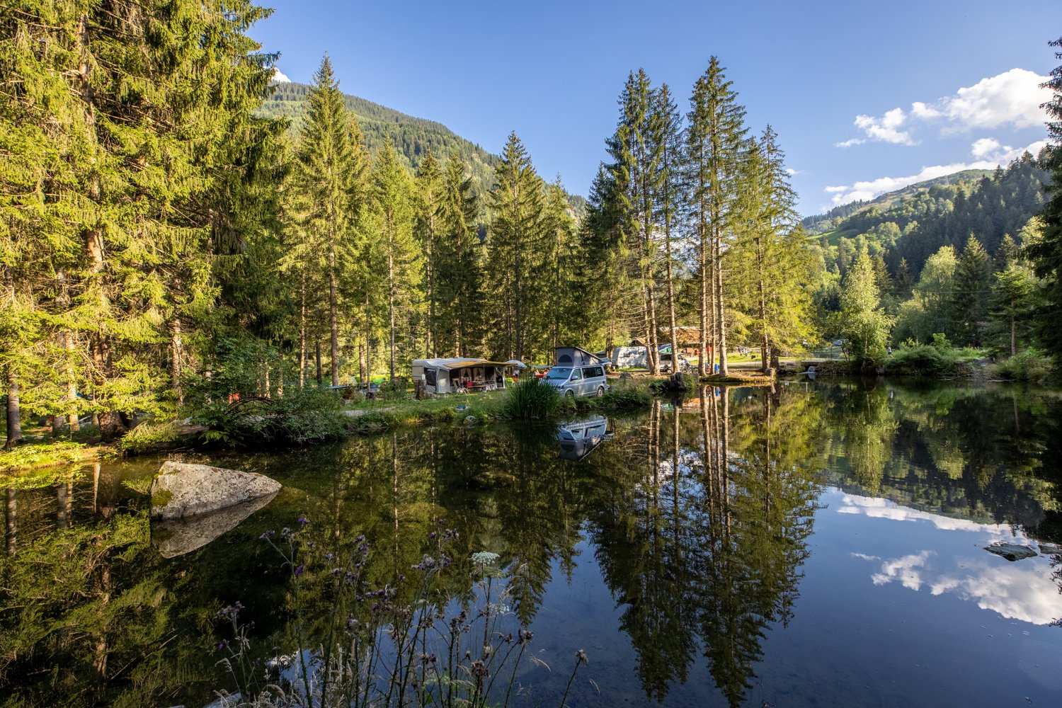 A small bathing lake with campers on the shore in the forest.